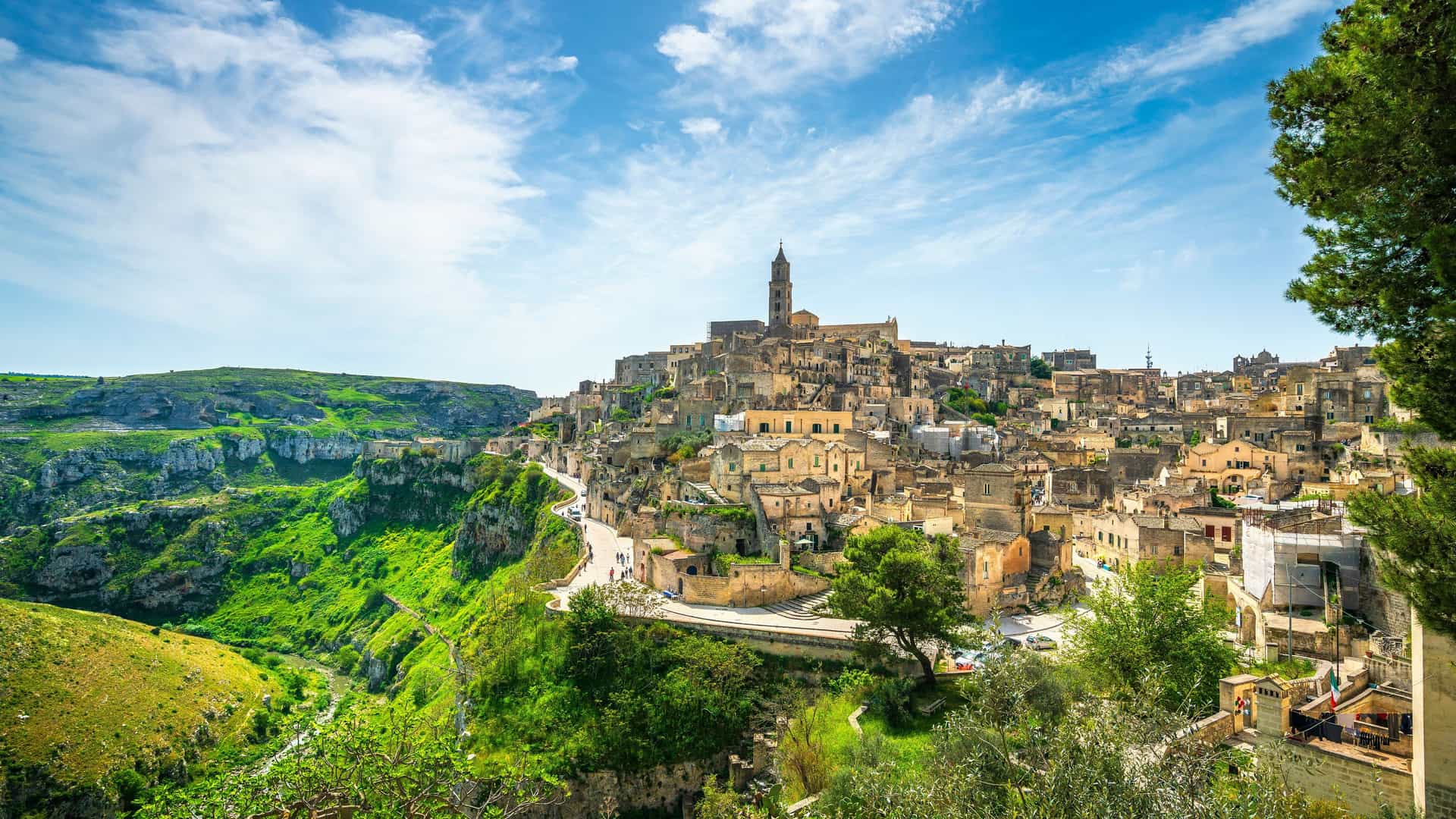 "A stunning panoramic view of the ancient Sassi di Matera cave dwellings in Matera, Italy, with the historic city perched on a hillside and a deep gorge beside it. "