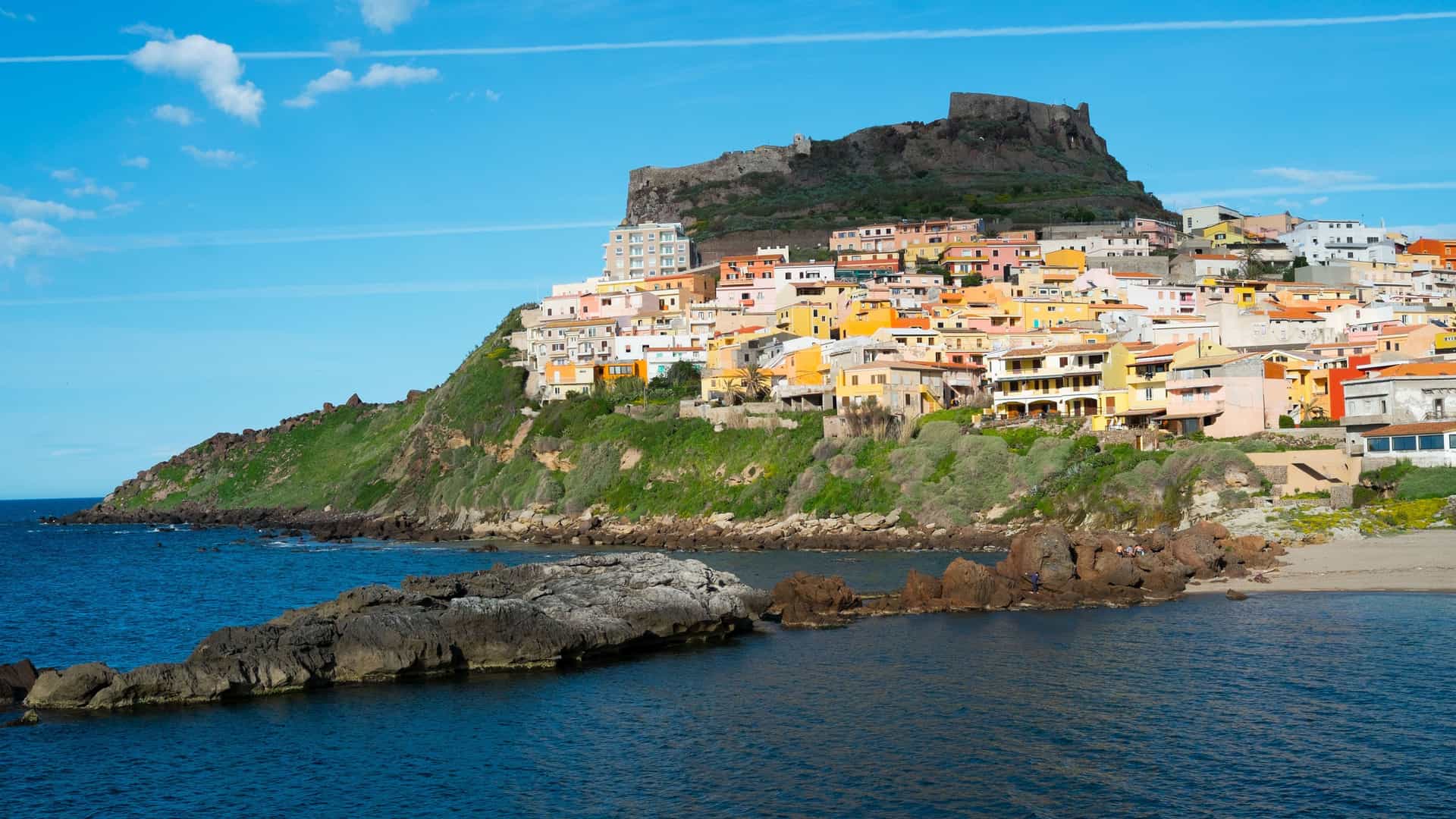 A stunning view of Castelsardo, Sardinia, with a medieval castle perched on a rocky promontory overlooking a colorful town cascading down to the sea.