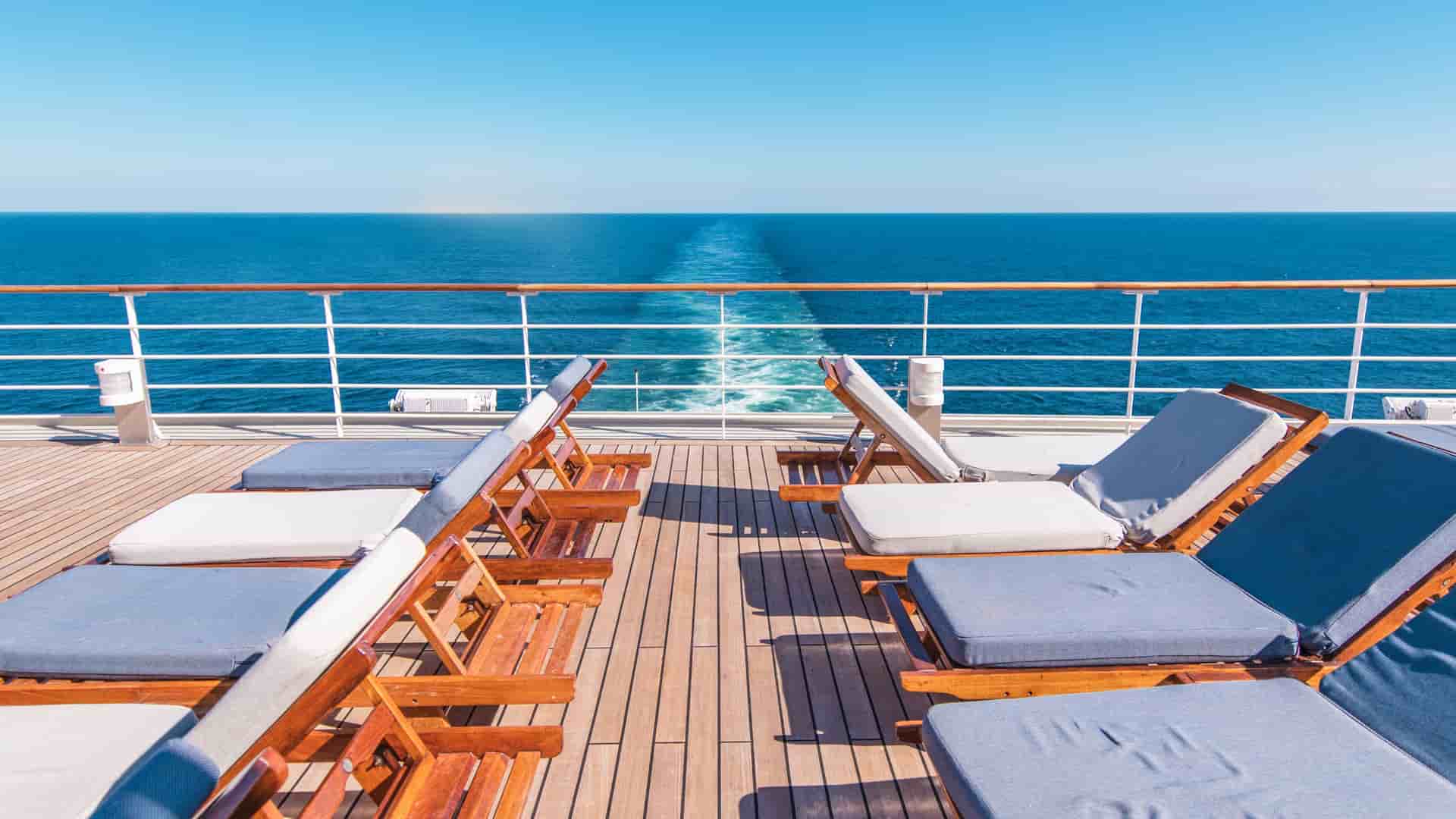 Two rows of lounge chairs on a cruise ship deck during a bright, sunny day.