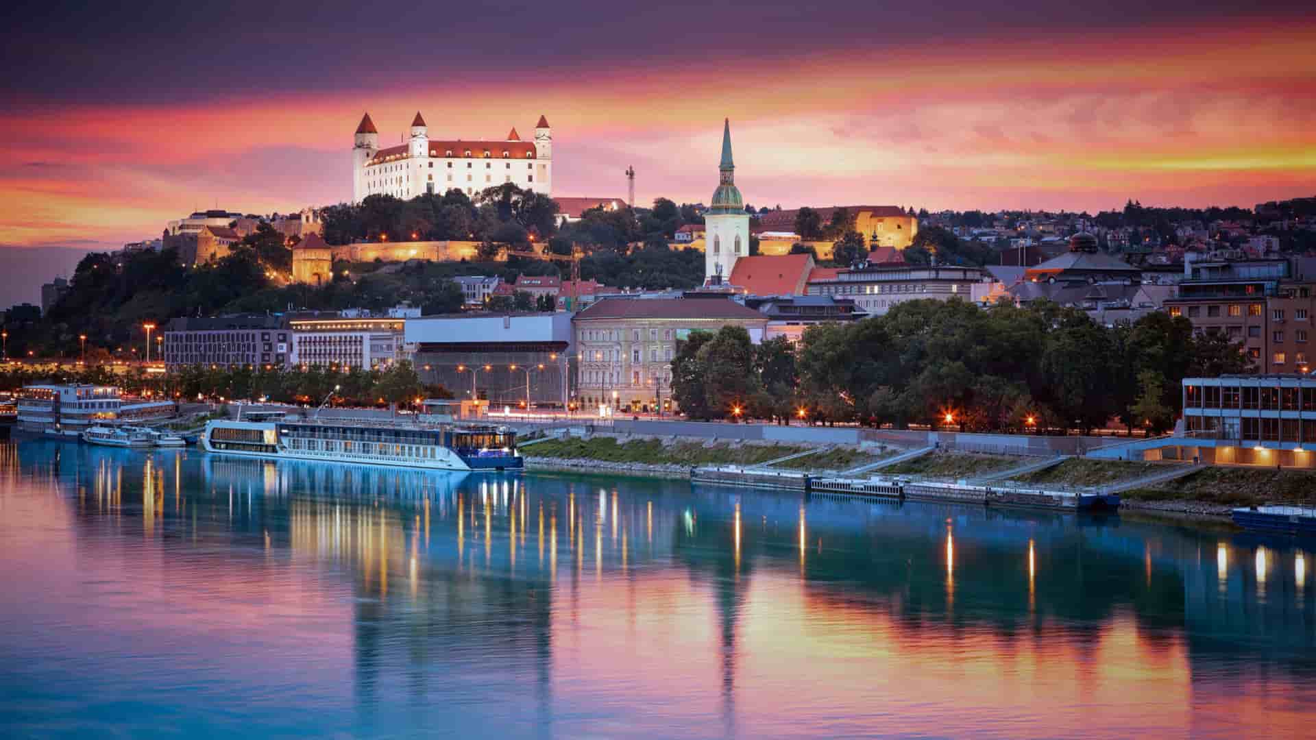 An AmaWaterways river ship cruises through the Danube on the "Best of the Danube" itinerary, as the sun sets and creates a purple hue in the sky.