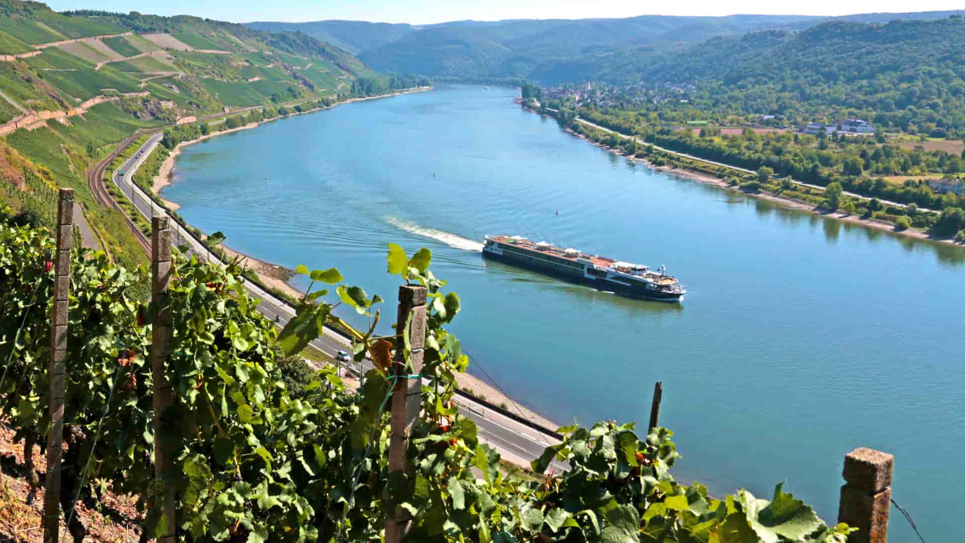  A scenic view of an Avalon Waterways ship cruising along the Rhine River in Germany, with lush green vineyards on the hillsides.