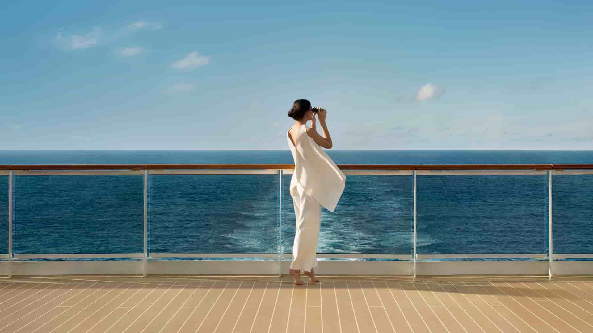 A woman wearing all white using binoculars to view the ocean.