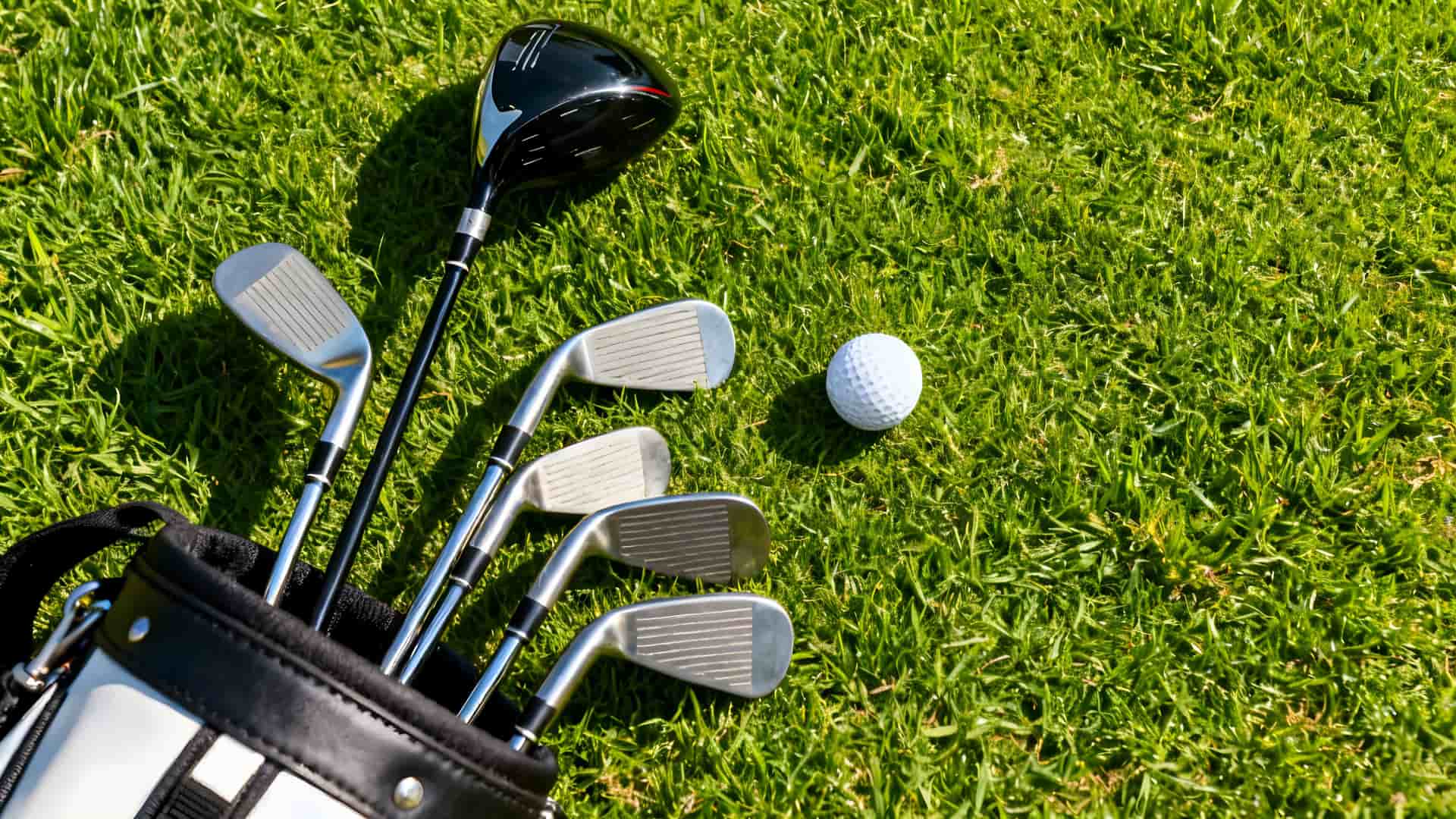 A set of golf clubs and a golf ball laying on bright green grass.