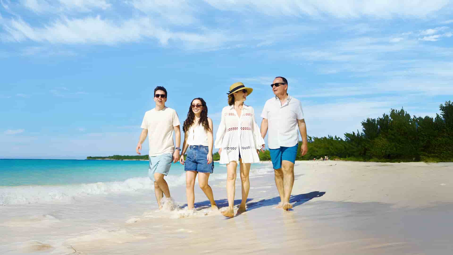 A family of four walks along the white-sand beach of Half Moon Cay in the Bahamas, enjoying a sunny Caribbean day on their Holland America Line cruise.