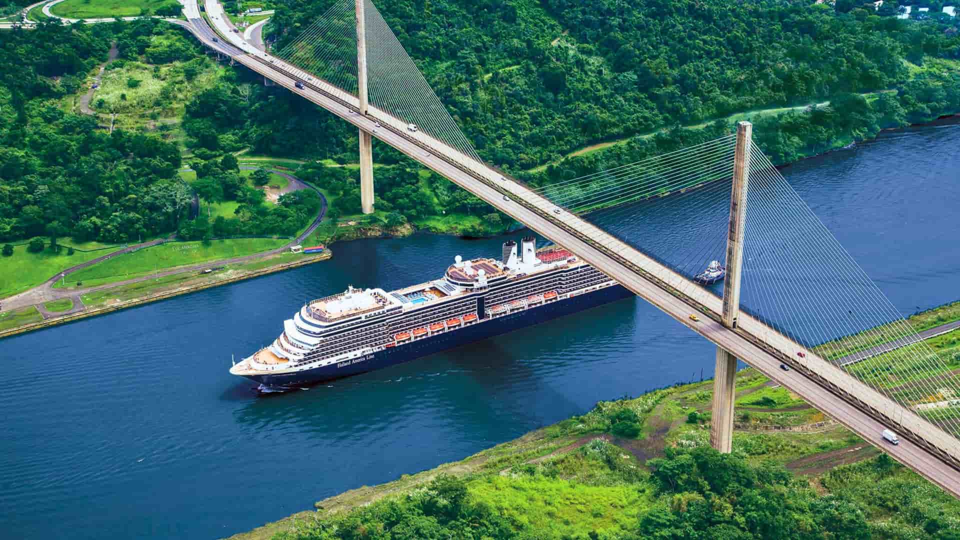   An aerial view of a Holland America cruise ship navigating through the Panama Canal under the Centennial Bridge, showcasing a world-famous transit in Panama.