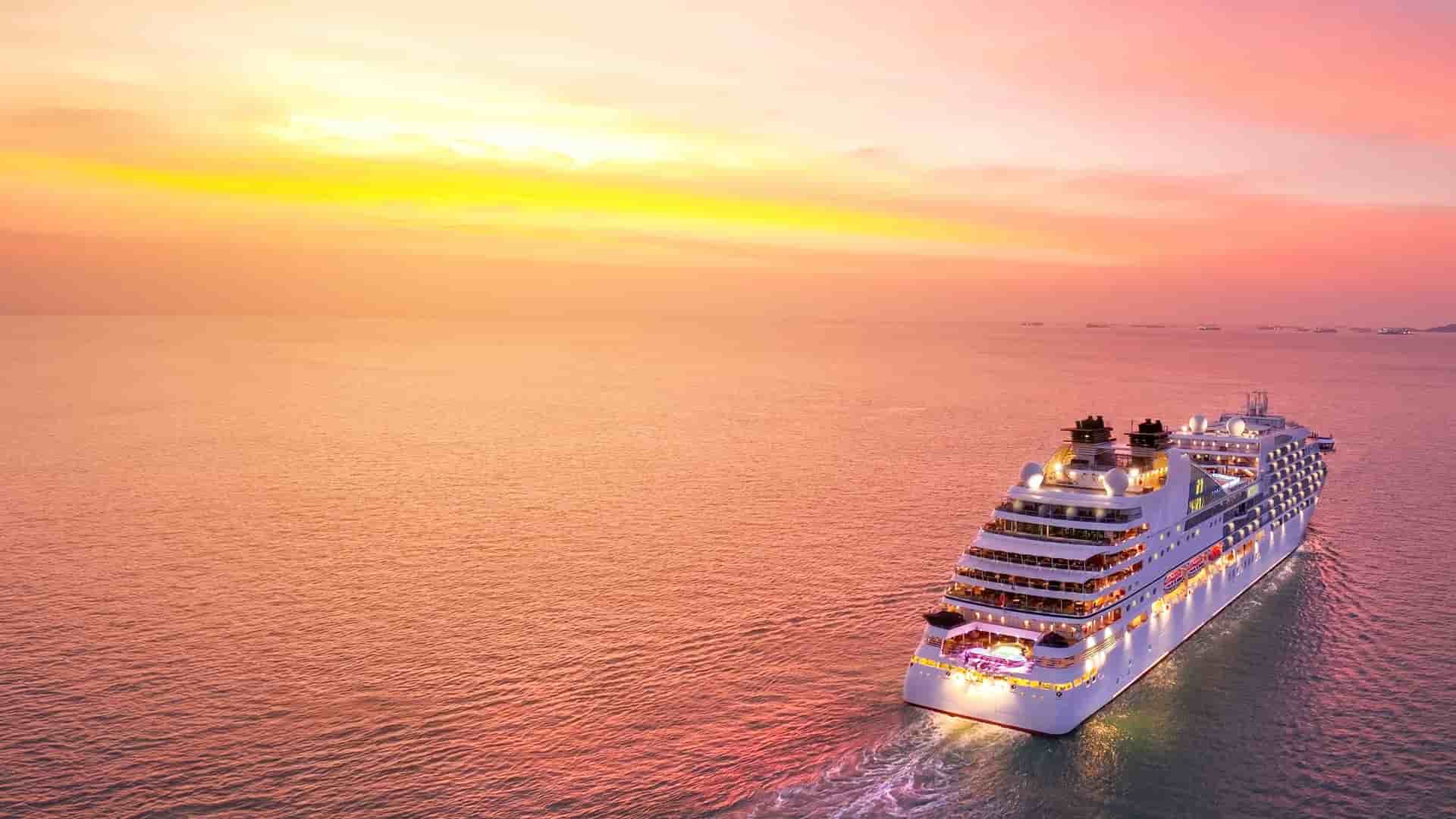 A wide shot image of a luxury cruise ship sailing away into the pink and orange sunset