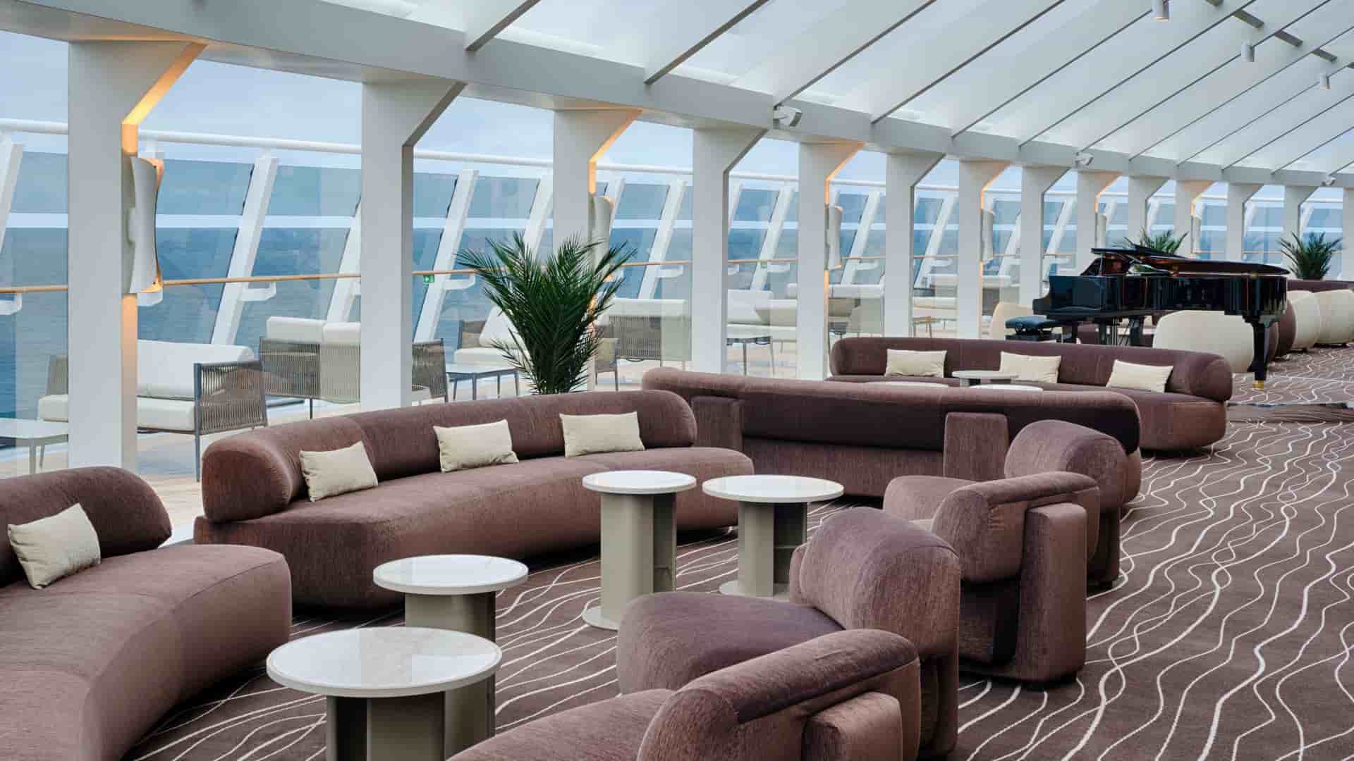 Dusty rose colored sofas in the MSC Yacht Clubs exclusive Top Sail Lounge, featuring mid-century modern decor and floor to ceiling windows.