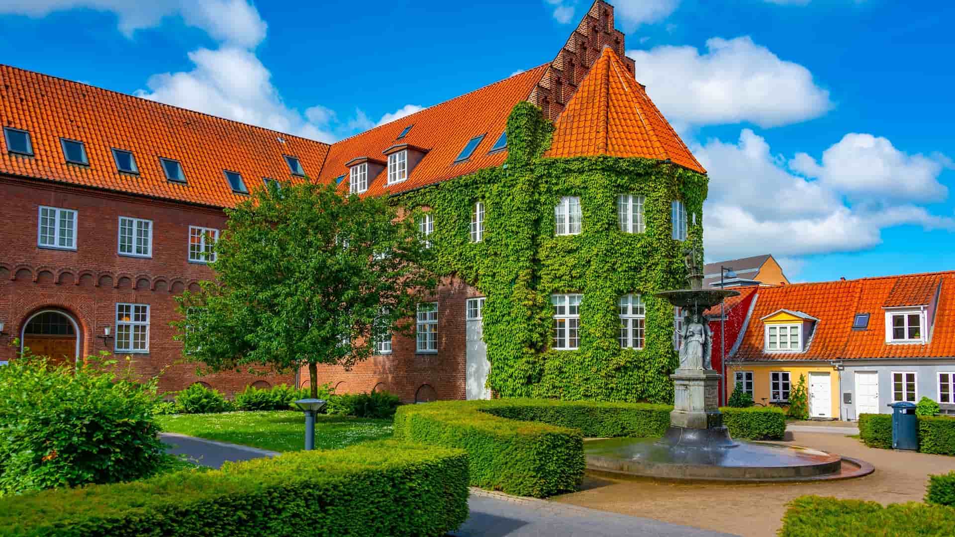 An outdoor courtyard with a fountain in front of the historic, ivy-covered Aalborghus Castle, a major landmark in the city.