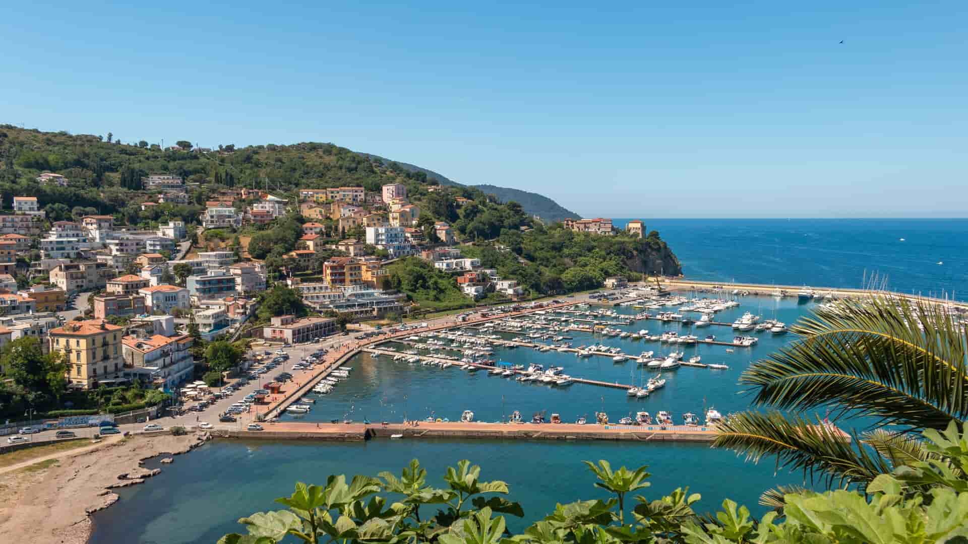 A high-angle view of the bustling Agropoli marina in Italy, with numerous boats moored in the harbor, surrounded by a picturesque town built into a green hillside.