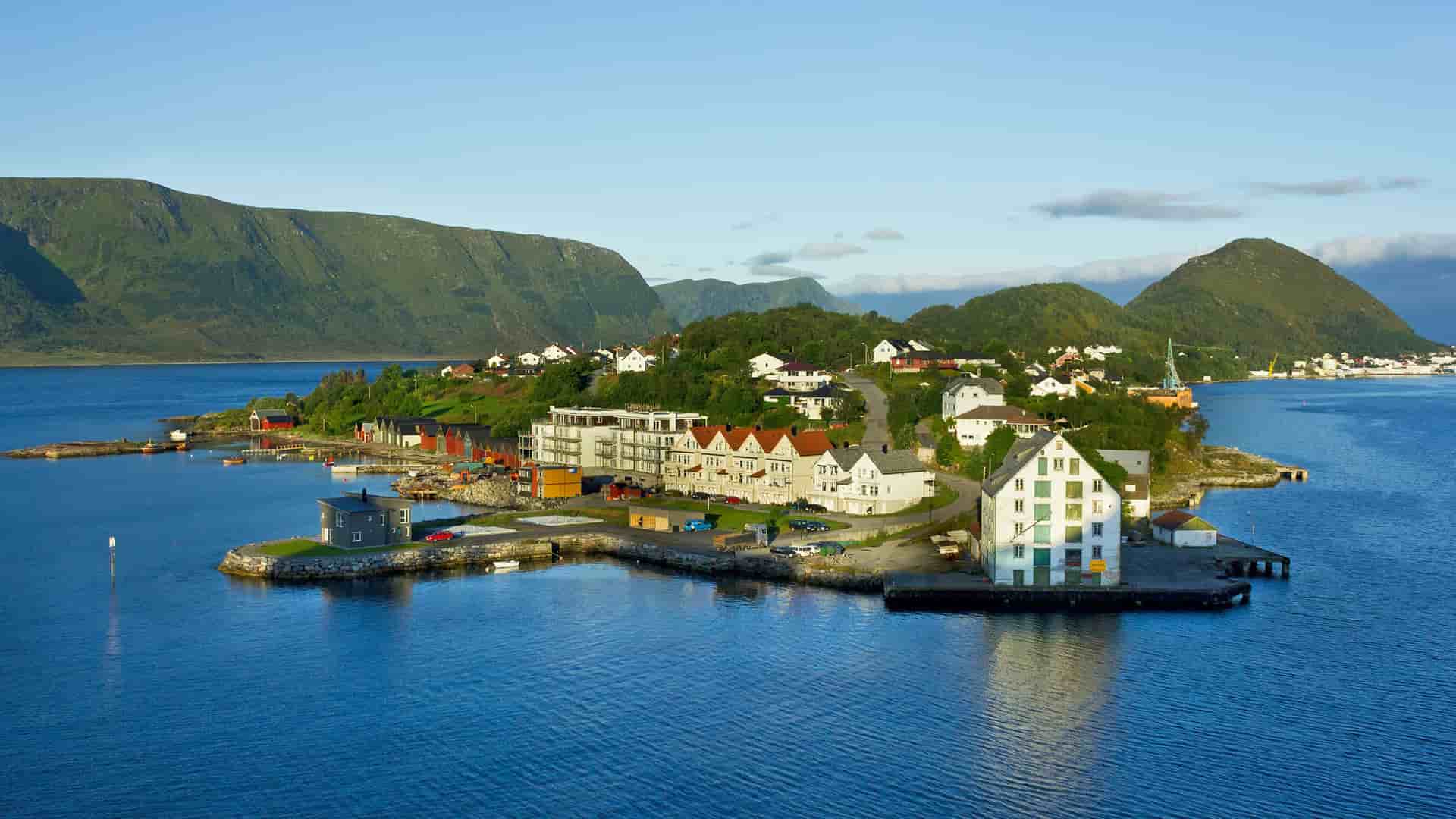 A tranquil shot of a small island with colorful houses and a port, surrounded by the deep blue sea and majestic mountains in the distance near Ålesund, Norway.