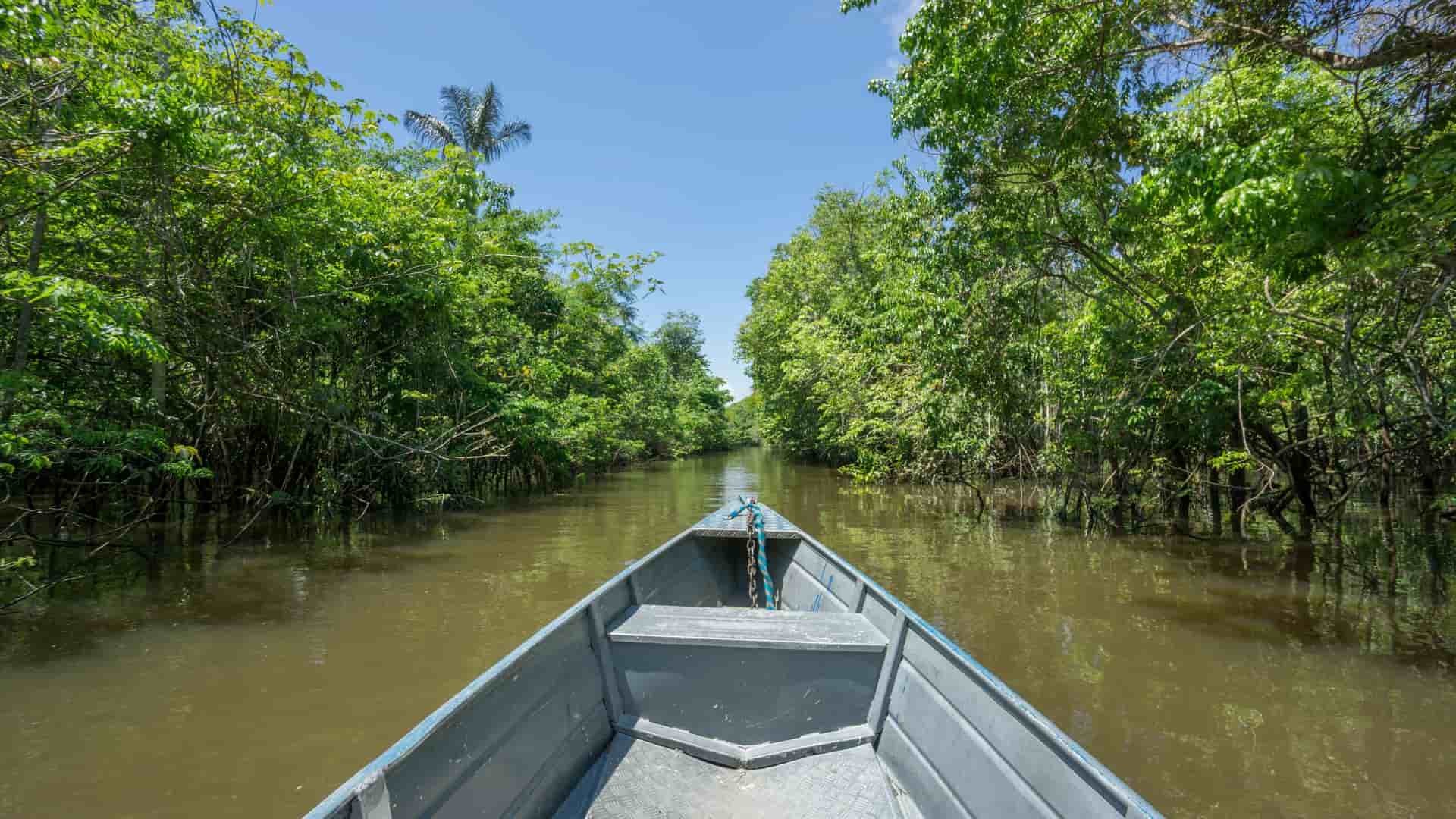 An aerial view of the vast Amazon River in Peru, meandering through a dense, green rainforest with a small floating lodge anchored along its banks.