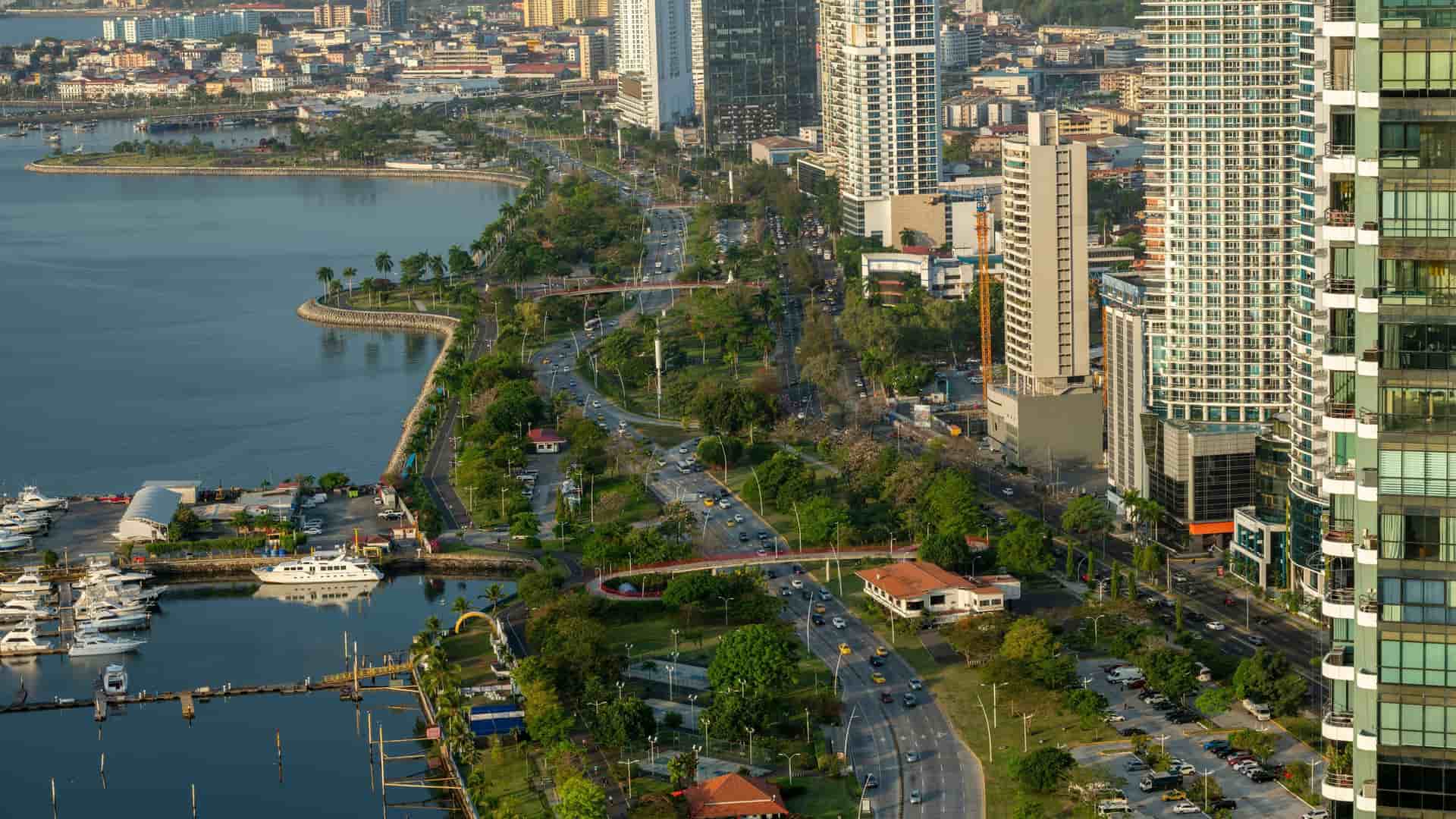 An aerial view of the bustling city of Balboa, Panama, with a scenic coastal road alongside a marina and tall modern skyscrapers in the background.