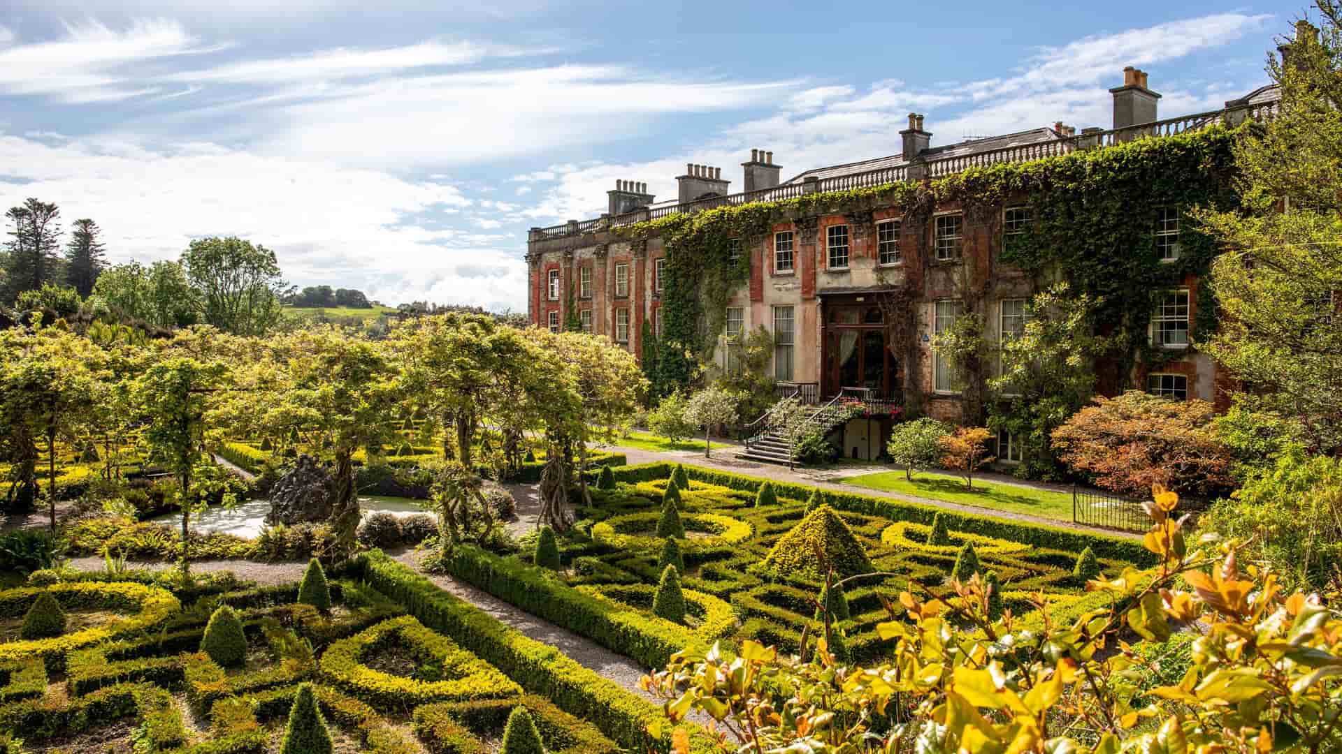 A beautiful garden with perfectly manicured hedges and trees in front of the grand Bantry House, a historic mansion in Bantry, Ireland.