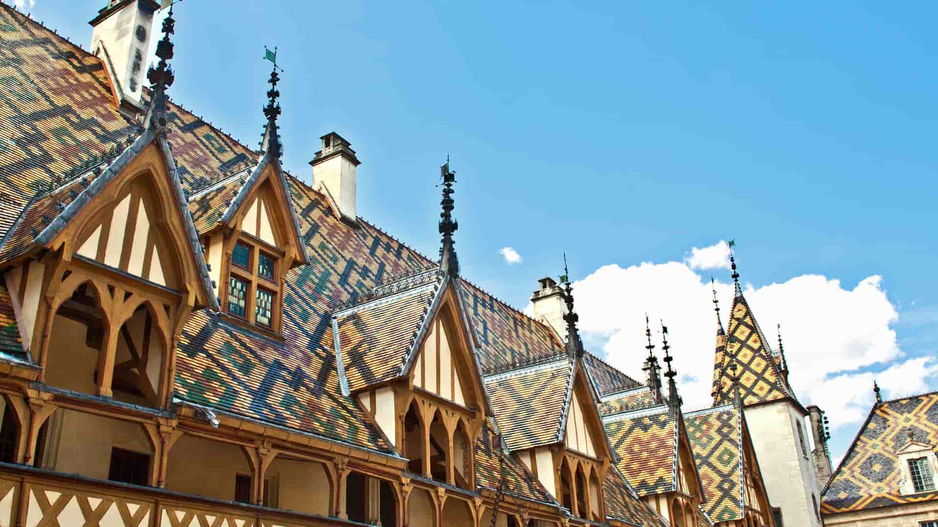 A detailed close-up of the multi-colored tiled roofs and architectural details of the historic Hospices de Beaune, a famous landmark in the Burgundy region of France.