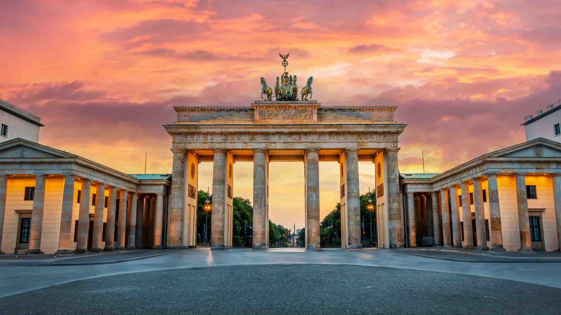 The famous Brandenburg Gate in Berlin, Germany, at sunrise, with a stunning orange and pink sky.