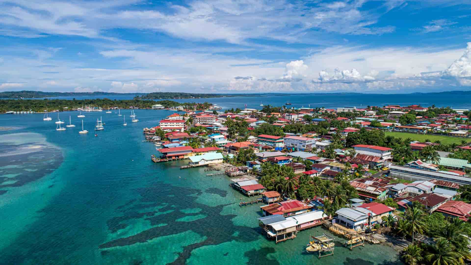 An aerial view of Bocas del Toro, a vibrant town on the Caribbean coast of Panama, featuring colorful houses built over clear blue water and numerous sailboats docked nearby.