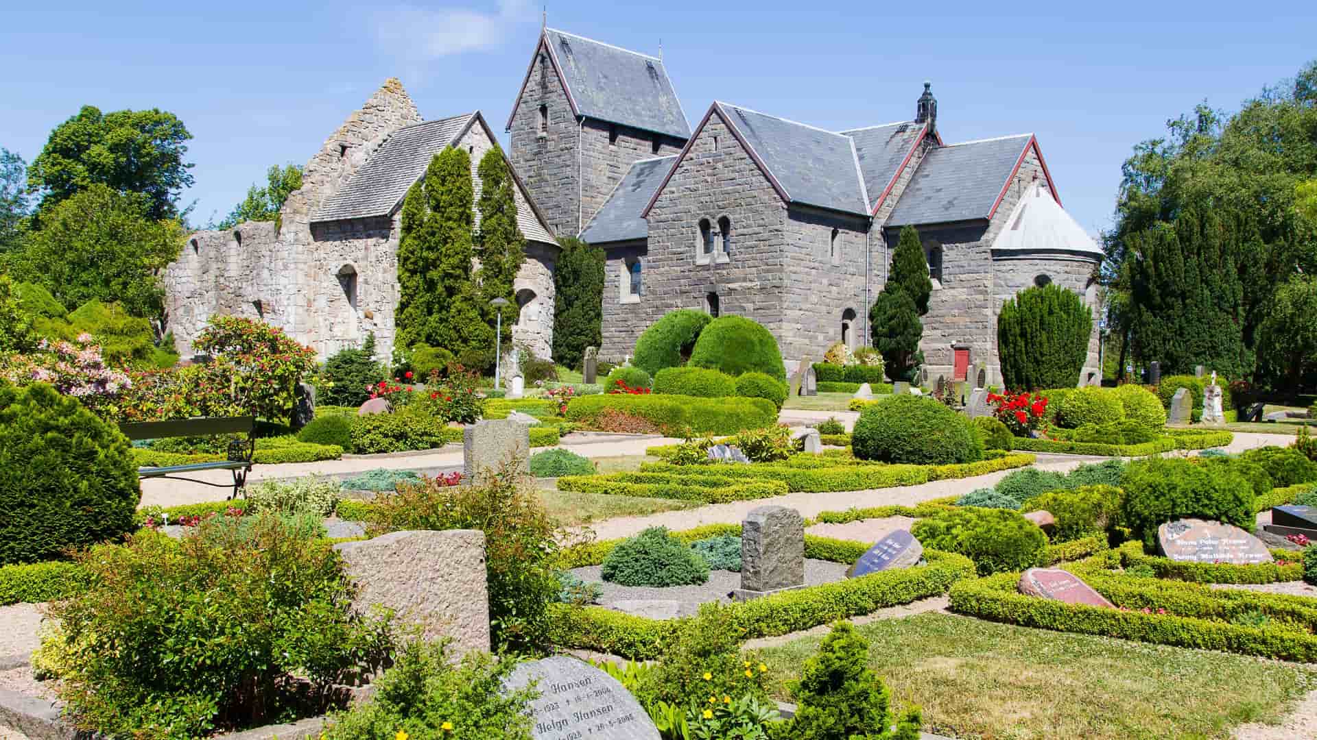 A stone church and cemetery on the Danish island of Bornholm, with well-maintained gardens and tombstones surrounding the historic, granite building.