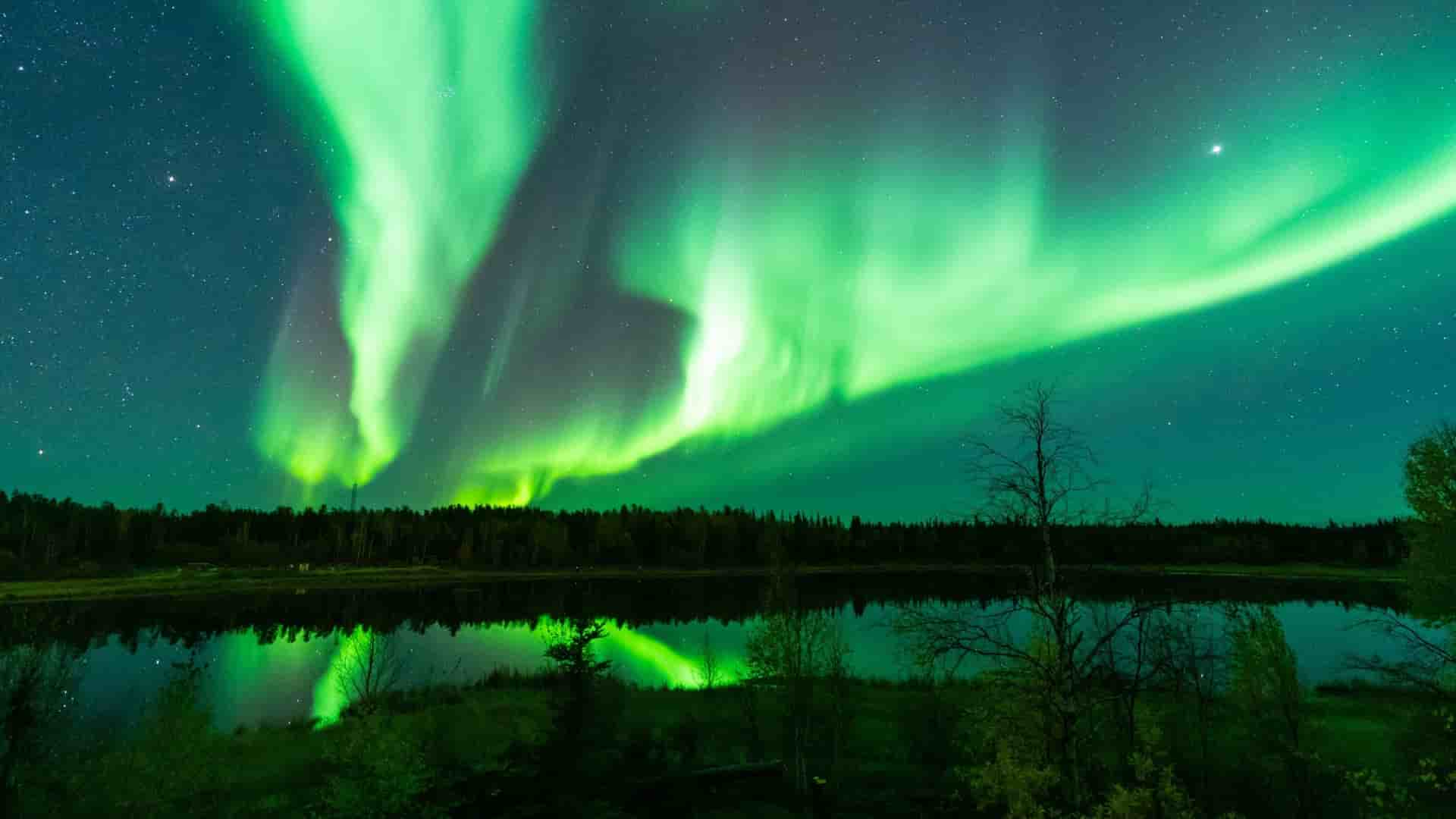 A mesmerizing long-exposure photograph of the vibrant green Aurora Borealis, also known as the Northern Lights, illuminating the night sky and reflecting on a calm lake in the Canadian Arctic.
