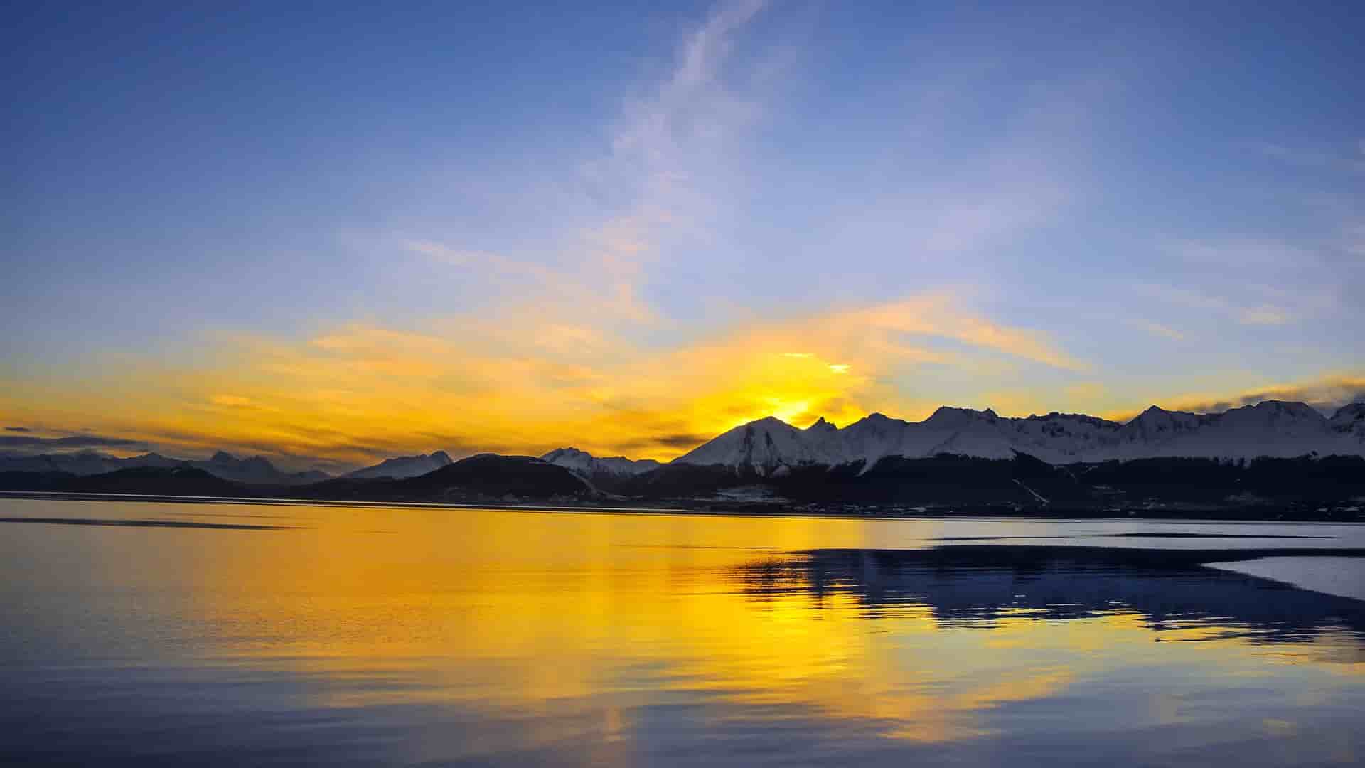 A beautiful sunrise over the snow-capped mountains of Cape Horn, with the water reflecting the vibrant orange and yellow hues of the sky.