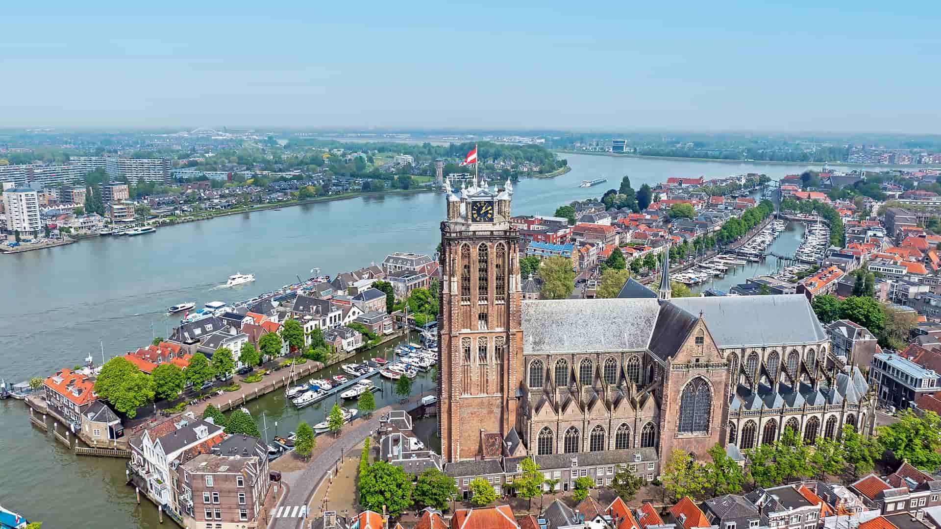 An aerial view of the historic Dutch city of Dordrecht, showcasing the iconic Grote Kerk and its bell tower overlooking a bustling network of rivers and canals.
