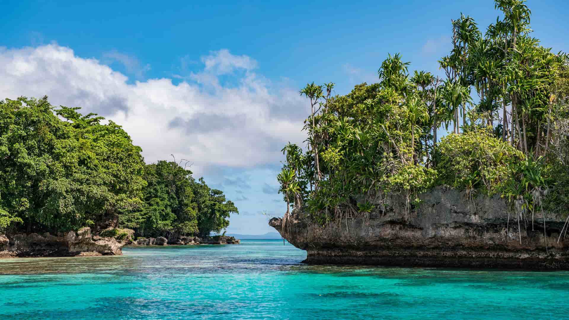 A tropical view of Duke of York Island in Papua New Guinea, with dense green vegetation on rocky islets surrounded by stunning turquoise water under a blue sky.