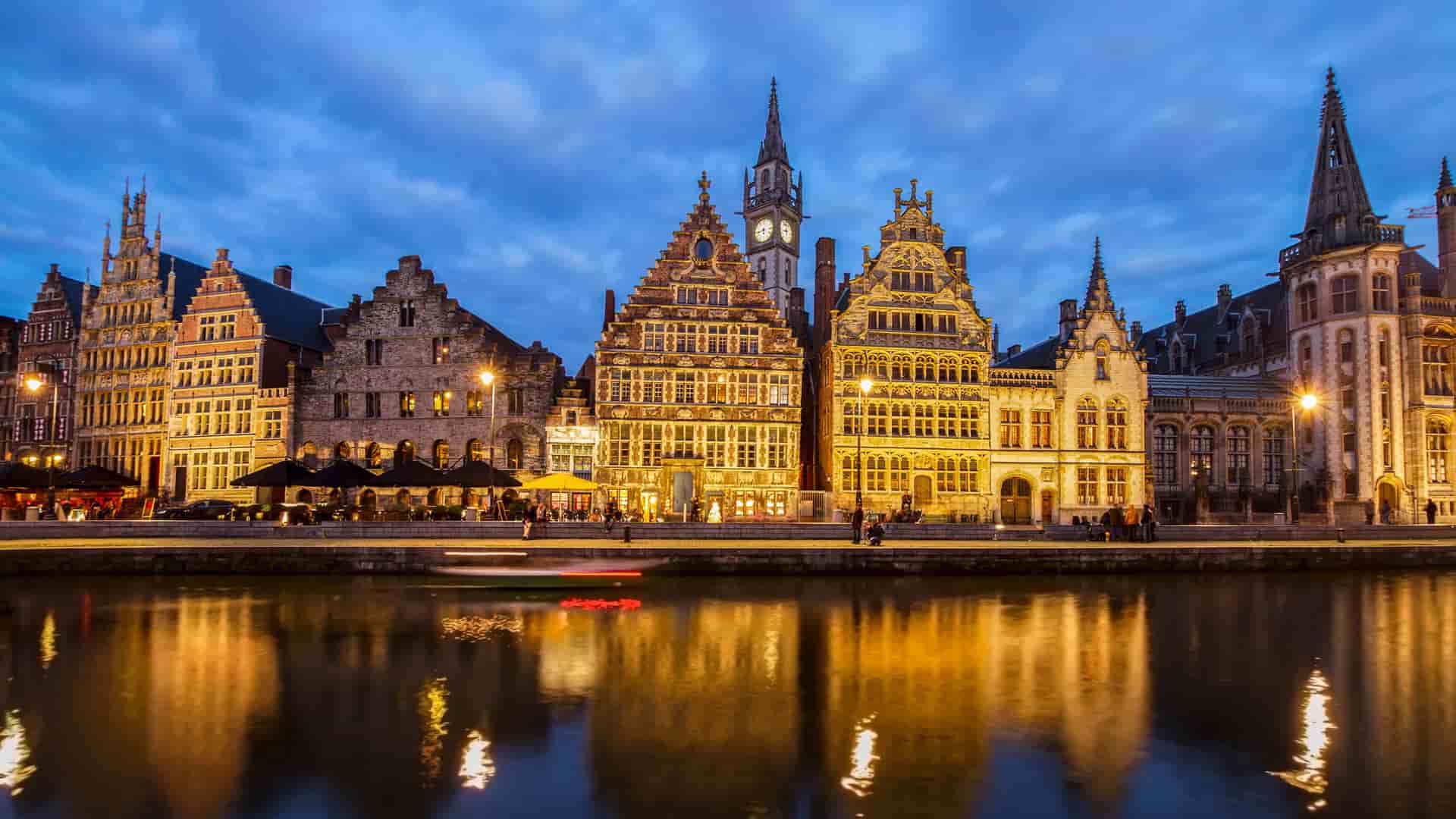 A picturesque evening view of the Graslei and Korenlei in Ghent, Belgium, showcasing the illuminated historic medieval buildings reflected in the Lys River.