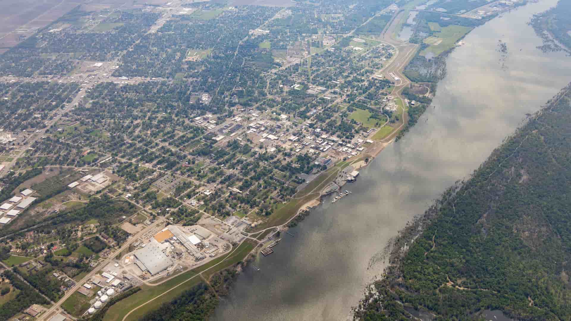"An aerial view of Greenwood, Mississippi, showing the city's grid-like street layout, the Yazoo River with its curving banks, and the surrounding green landscape and farmland.  "