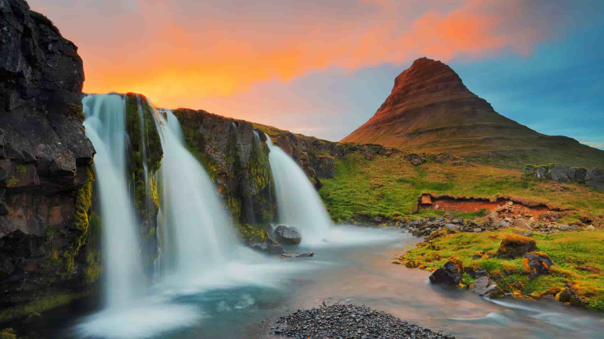 A long-exposure shot of the Kirkjufellsfoss waterfall cascading down the cliffside with the iconic Kirkjufell mountain in the background at sunset in Grundarfjörður, Iceland.