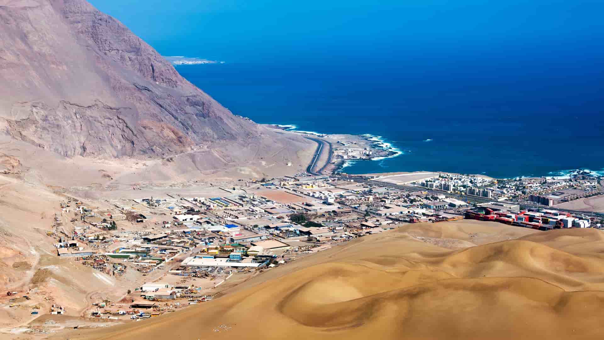 A scenic high-angle view of the port city of Iquique, Chile, nestled between the Pacific Ocean and a large arid mountain.
