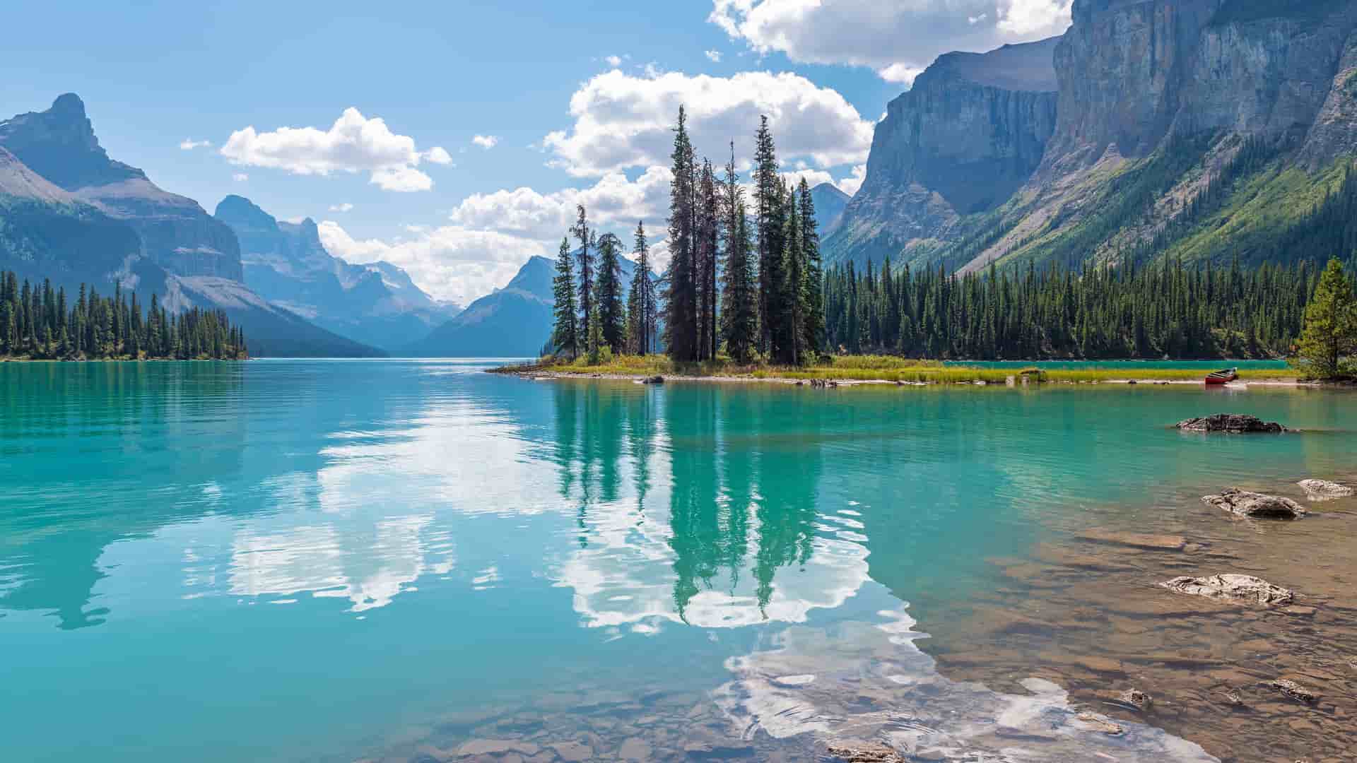 "A scenic view of Spirit Island with a cluster of pine trees in the middle of the turquoise blue waters of Maligne Lake, surrounded by the rocky Canadian Rockies mountains in Jasper National Park.  "
