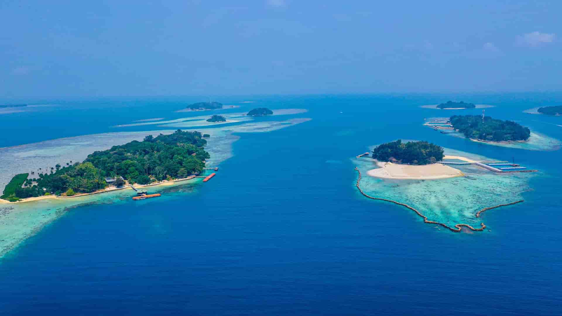 An aerial view of small, tropical islands surrounded by a stunning coral reef and calm, crystal-clear turquoise water in the Java Sea.