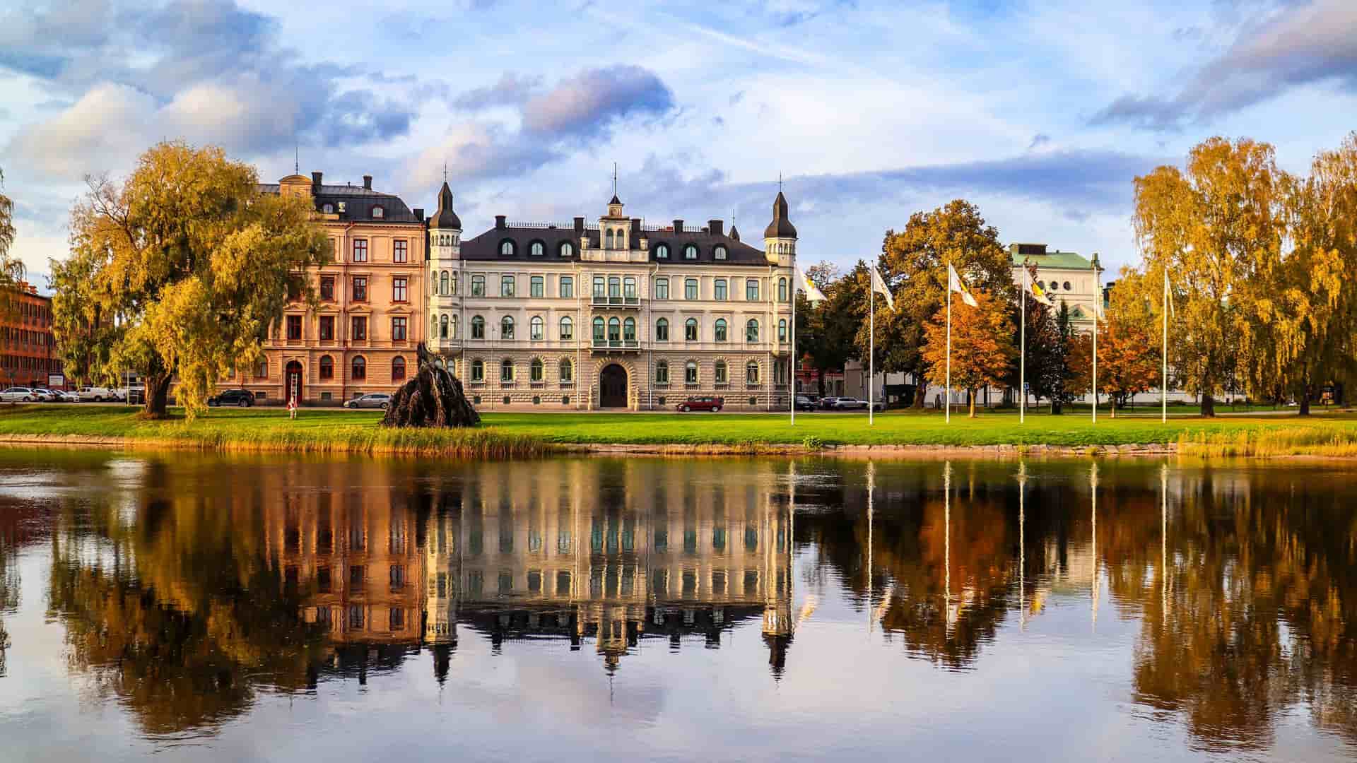 "A scenic autumn shot of the historic Värmlands Museum, a large white building with a castle-like design, reflecting beautifully in the waters of the Klarälven River in Karlstad, Sweden.  "