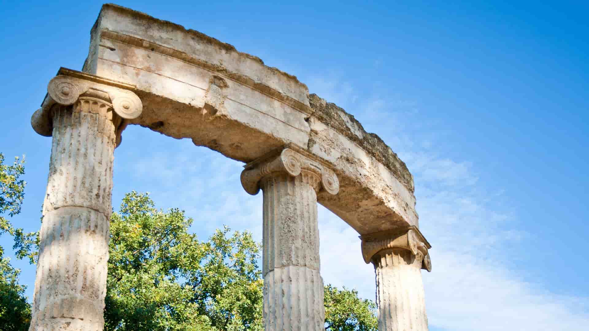 Looking up at the ancient stone columns of the Philippeion, with their distinctive scroll-like Ionic capitals, in the ruins of Olympia, near Katakolon, Greece.