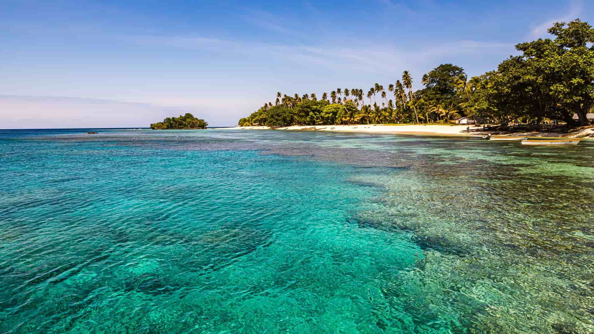 A tropical paradise on Kiriwina Island, with a pristine white sand beach, lush palm trees, and crystal-clear turquoise waters revealing a vibrant coral reef beneath.