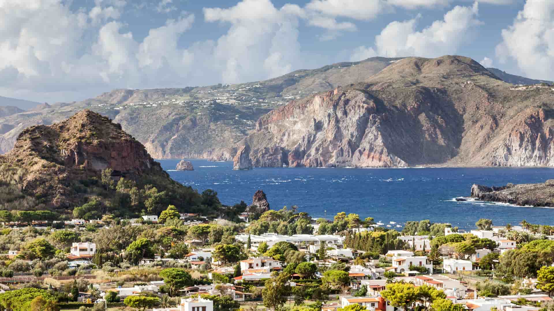 A stunning view of Lipari, the largest of the Aeolian Islands, showcasing the vibrant blue Tyrrhenian Sea, dramatic cliffs, and the whitewashed buildings of the resort town.