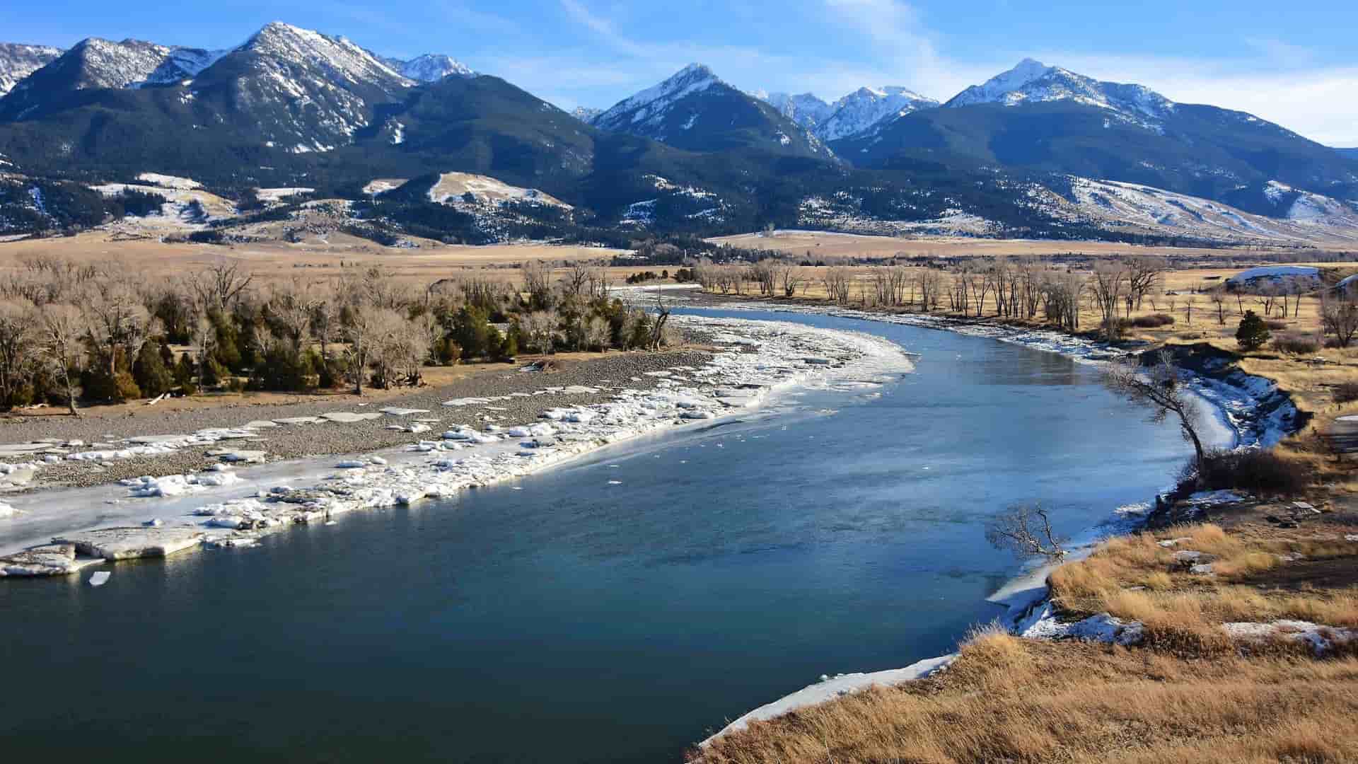 "A stunning winter landscape of the Yellowstone River near Livingston, Montana, with snow-capped mountains in the background and a frozen shoreline.  "