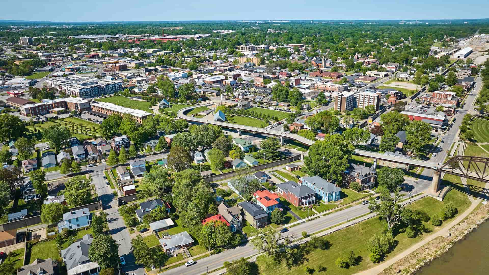 An aerial view of a large, complex highway interchange and a network of interstate roads in downtown Louisville, Kentucky. The roads, with sparse traffic, are seen approaching the Ohio River and the city's central business district and skyline.
