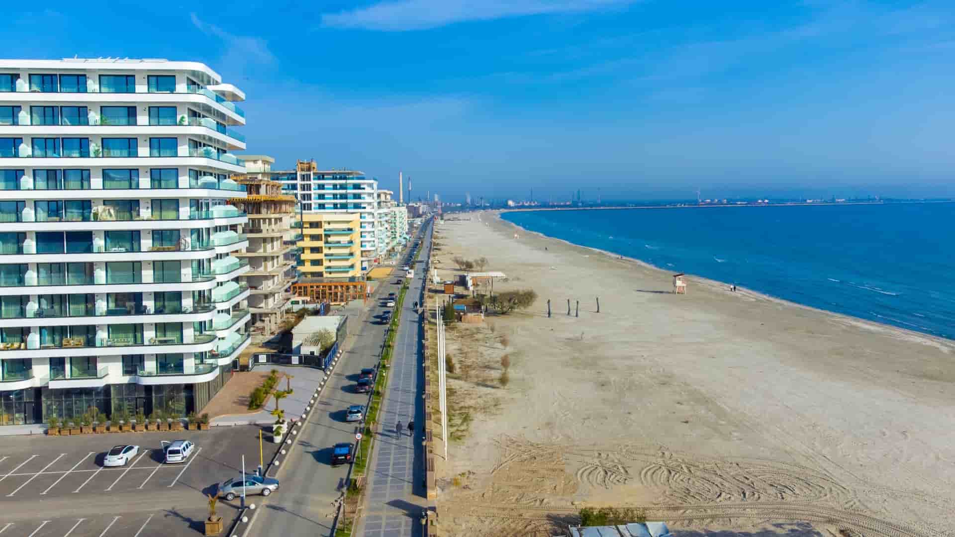 Modern, white high-rise apartments line the long, wide sandy beach and calm blue water in the resort of Mamaia, Romania.