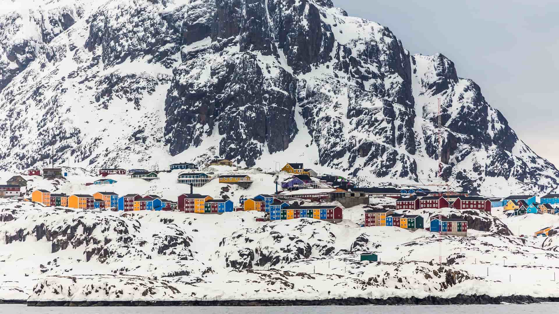 A stunning winter landscape of colorful houses nestled at the base of a massive snow-covered mountain in the remote town of Maniitsoq, Greenland.