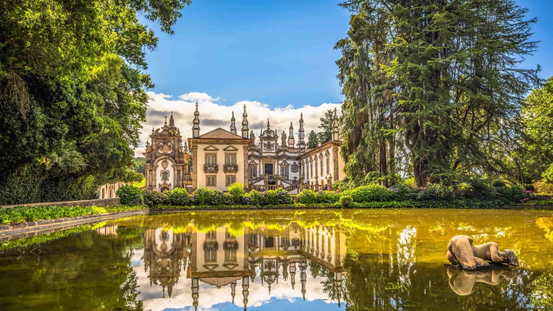 A picturesque view of the Baroque-style Casa de Mateus palace in Portugal, with its ornate facade and garden reflecting on a tranquil pond with a statue.