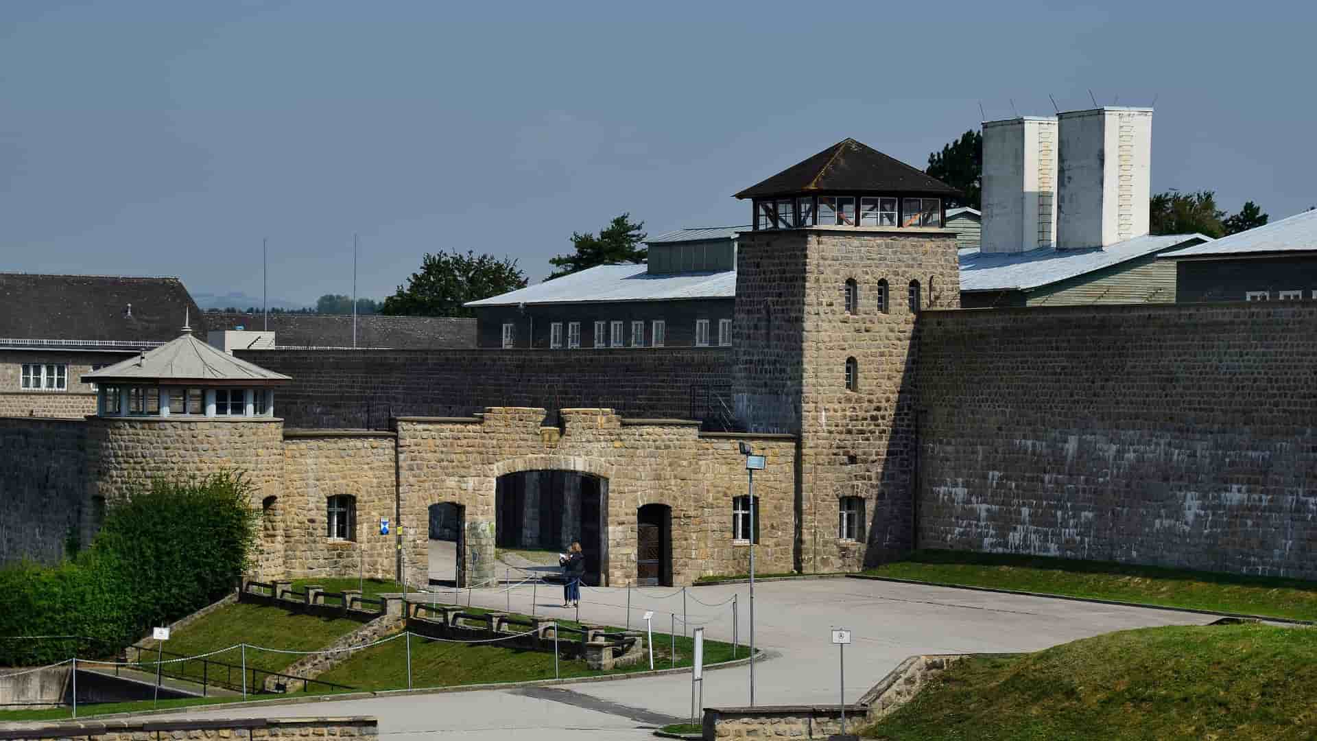 A historical view of the stone entrance gate, guard towers, and stone wall of the Mauthausen Concentration Camp memorial in Austria, a powerful and somber landmark.