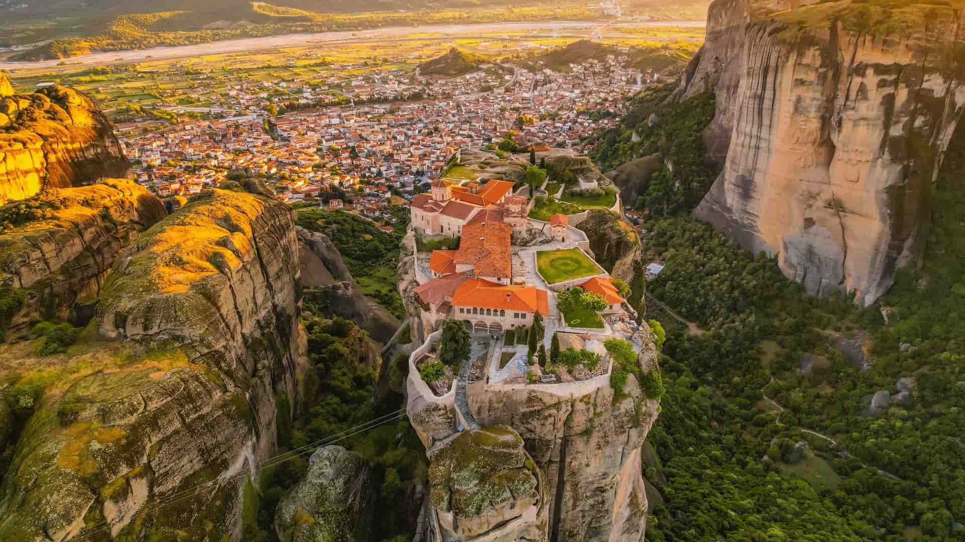 An incredible aerial shot of the Holy Monastery of the Transfiguration of Christ, also known as the Great Meteoron, perched on a massive rock pillar in Meteora, Greece.