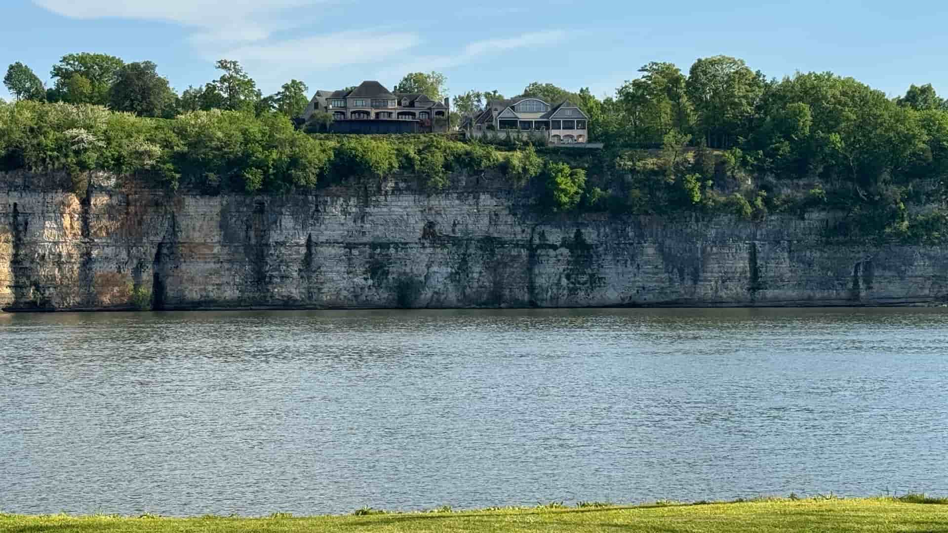 Houses stand on a lush, forested bluff overlooking a prominent limestone cliff and the water in the Muscle Shoals Area, Alabama.