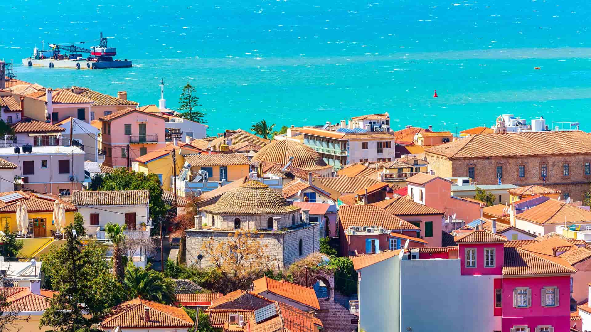 "A beautiful panoramic shot of the colorful, red-roofed buildings of Nafplio, Greece, with the deep blue waters of the Argolic Gulf in the background.  "