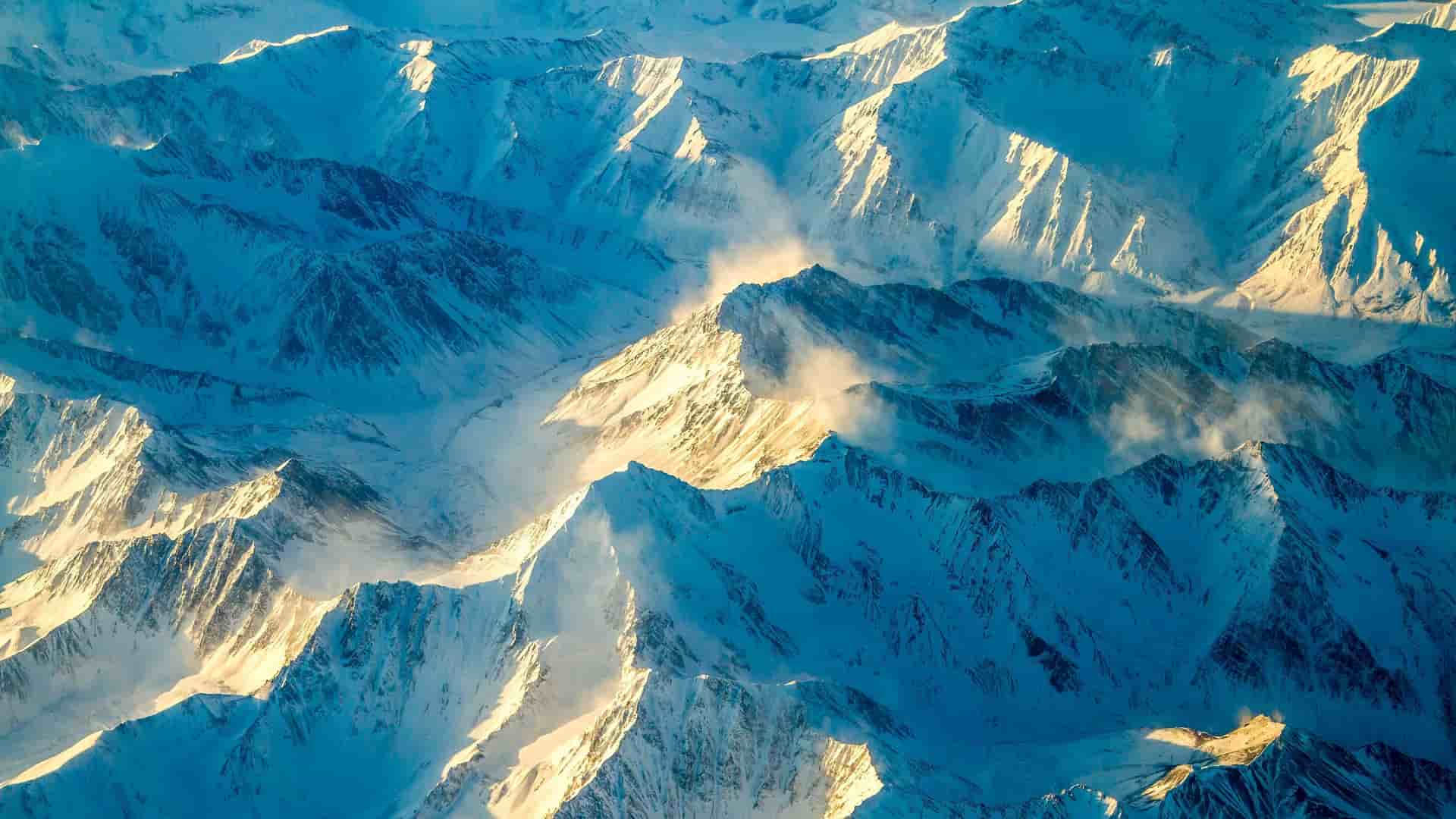 An aerial view of the snow-covered Kigluaik Mountains near Nome, Alaska, with dramatic peaks and valleys, casting long shadows in the late afternoon sun.
