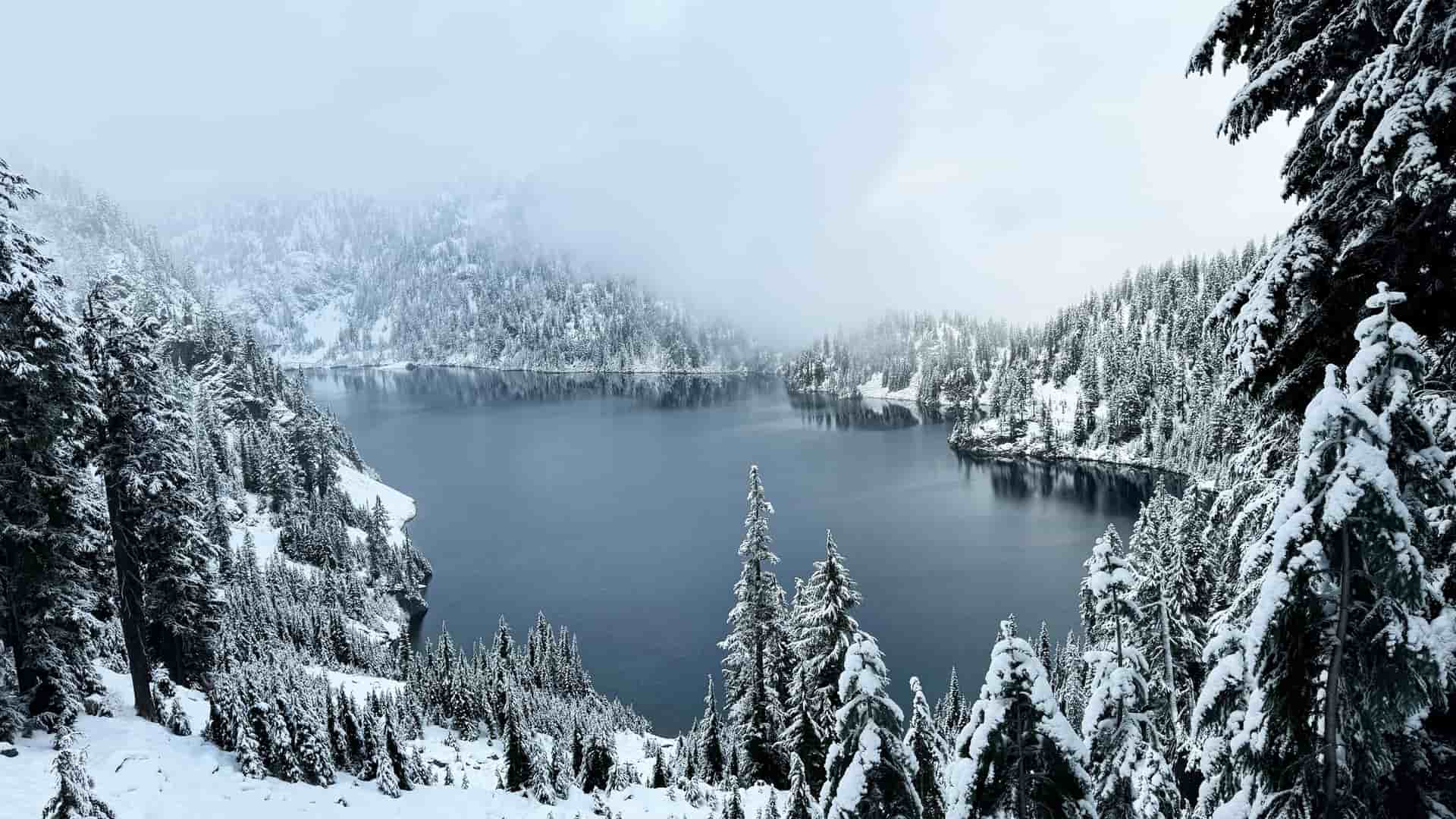 "A stunning panoramic shot of a serene winter landscape at Snow Lake, a popular hiking trail near North Bend, Washington, covered in fresh snow.  "