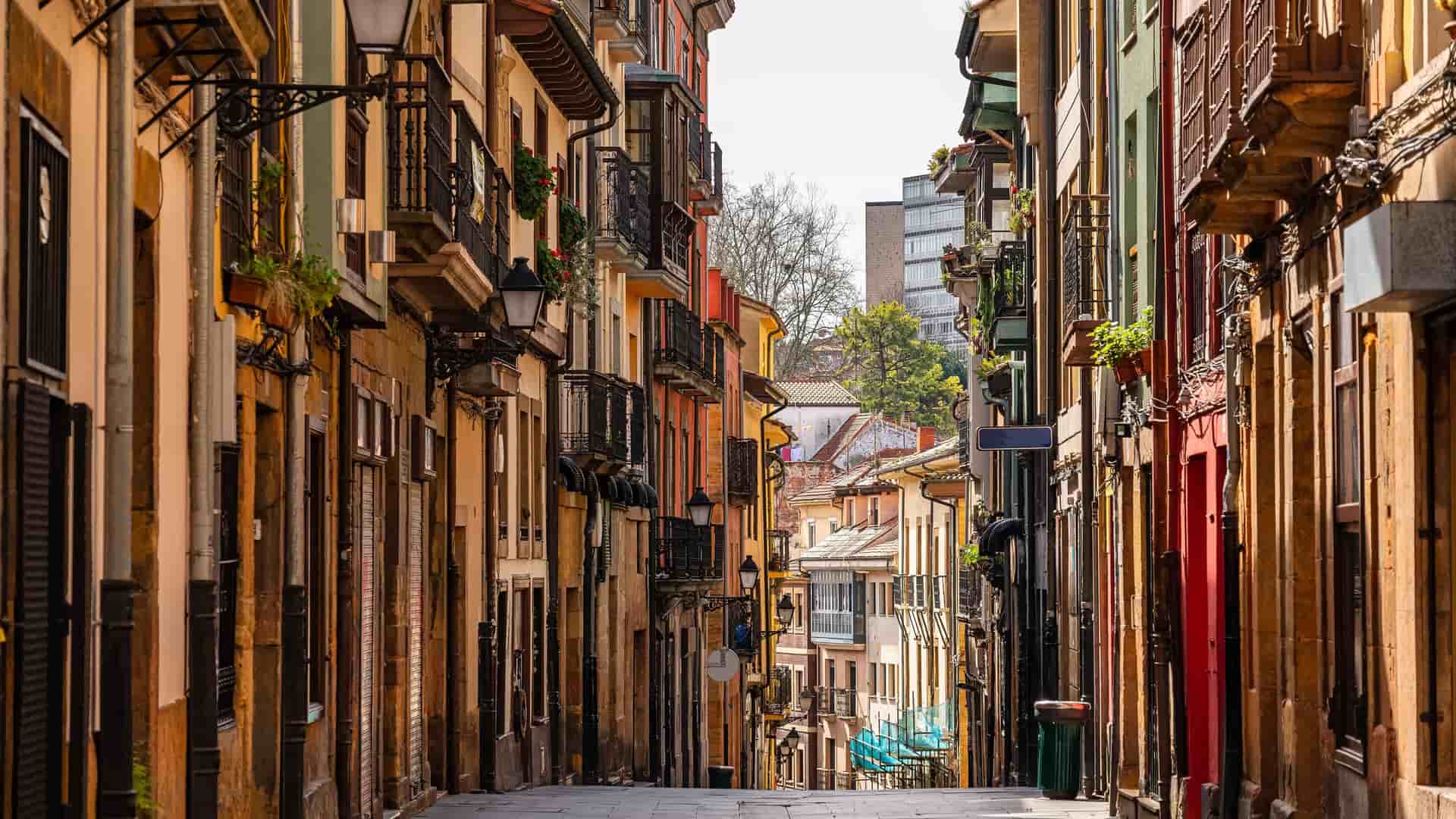 "A beautiful shot of a narrow cobblestone street in Oviedo, Spain, with historic buildings featuring colorful facades, balconies, and traditional lampposts.  "