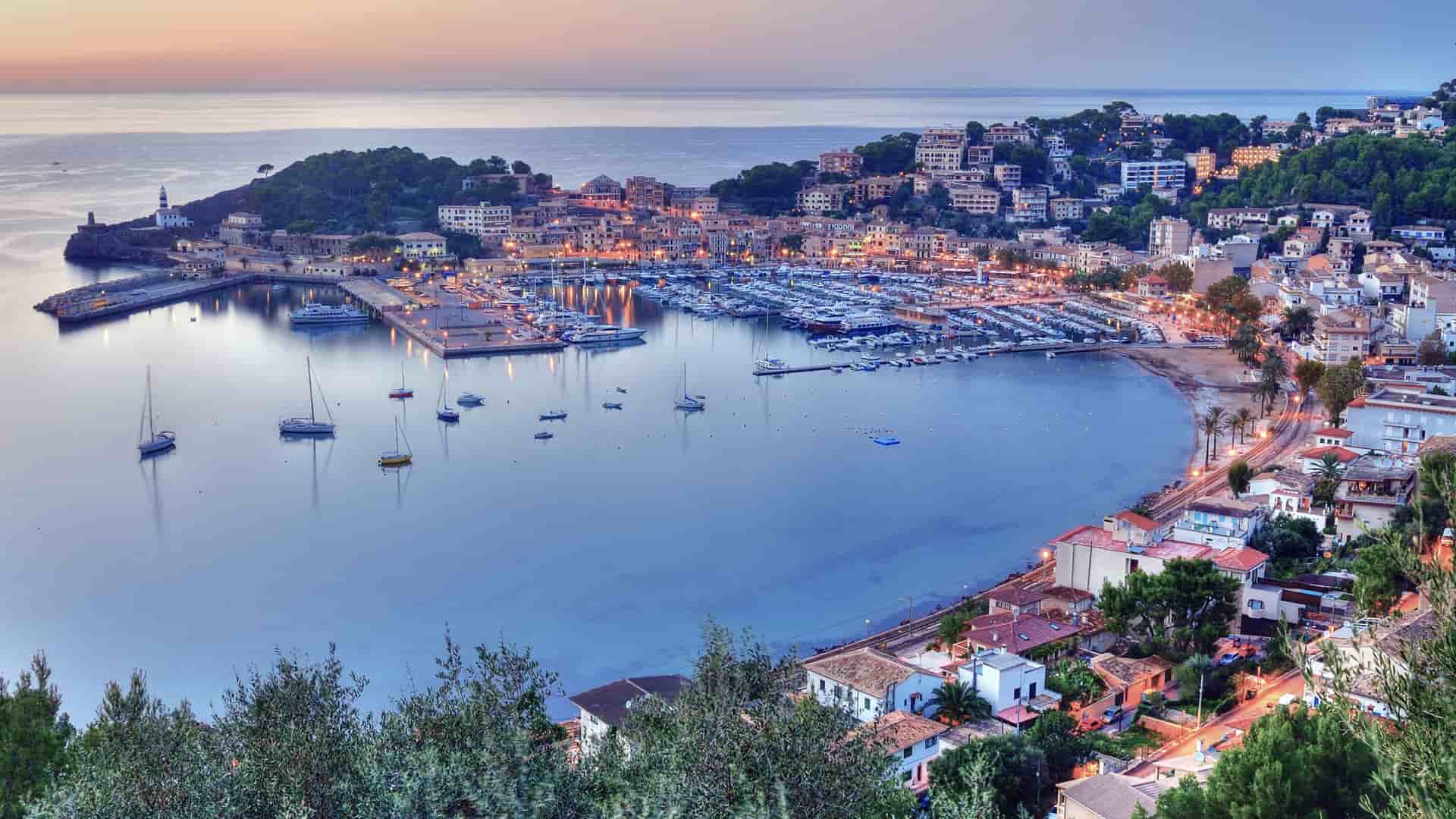 A panoramic sunset shot of the beautiful harbor in Palma de Mallorca, Spain, with a marina full of boats and buildings on the surrounding hills.