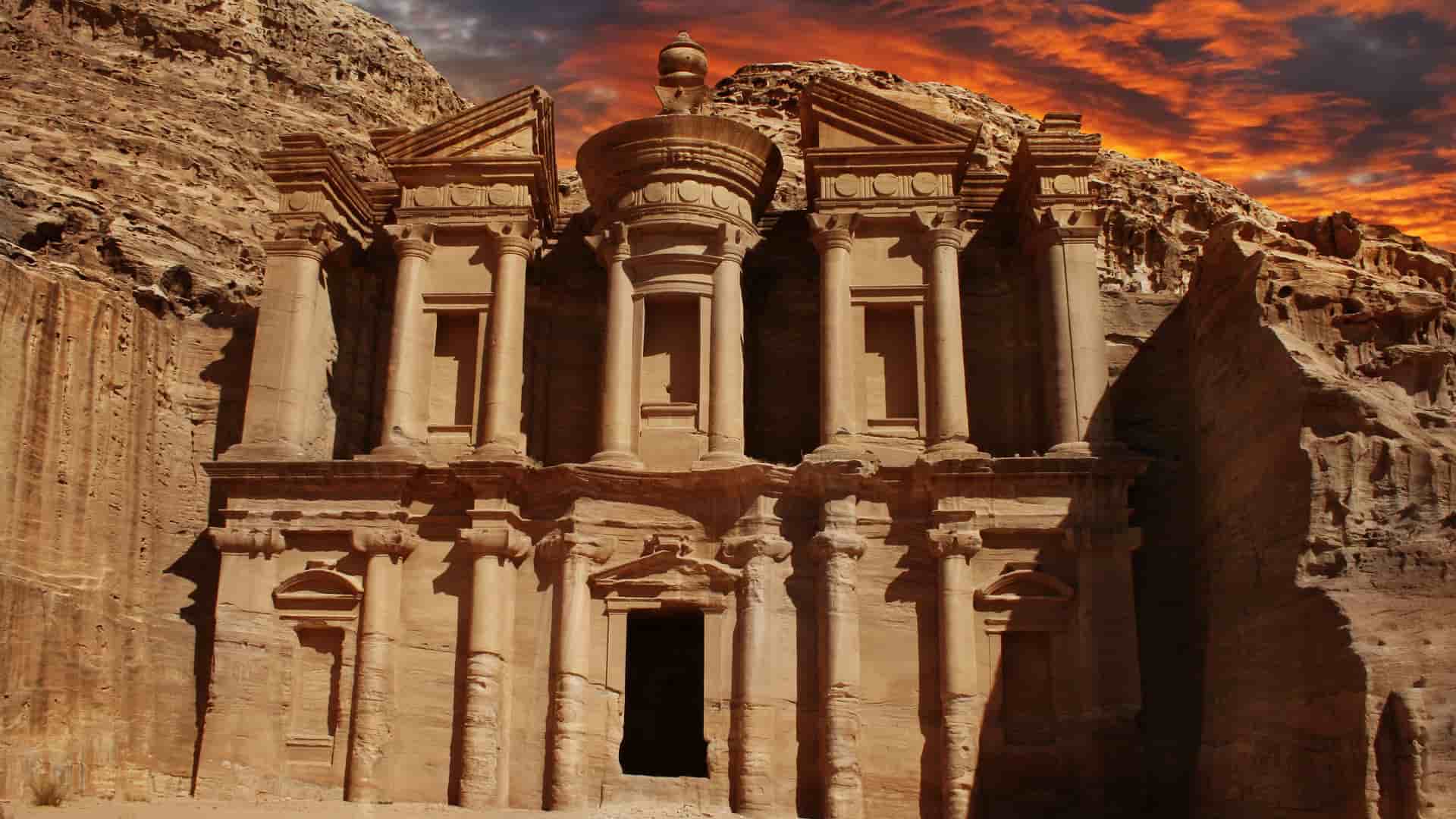 A stunning sunset view of the Ad-Dayr Monastery, a massive ancient tomb carved into a rock face, a historical landmark at the archaeological site of Petra, Jordan.