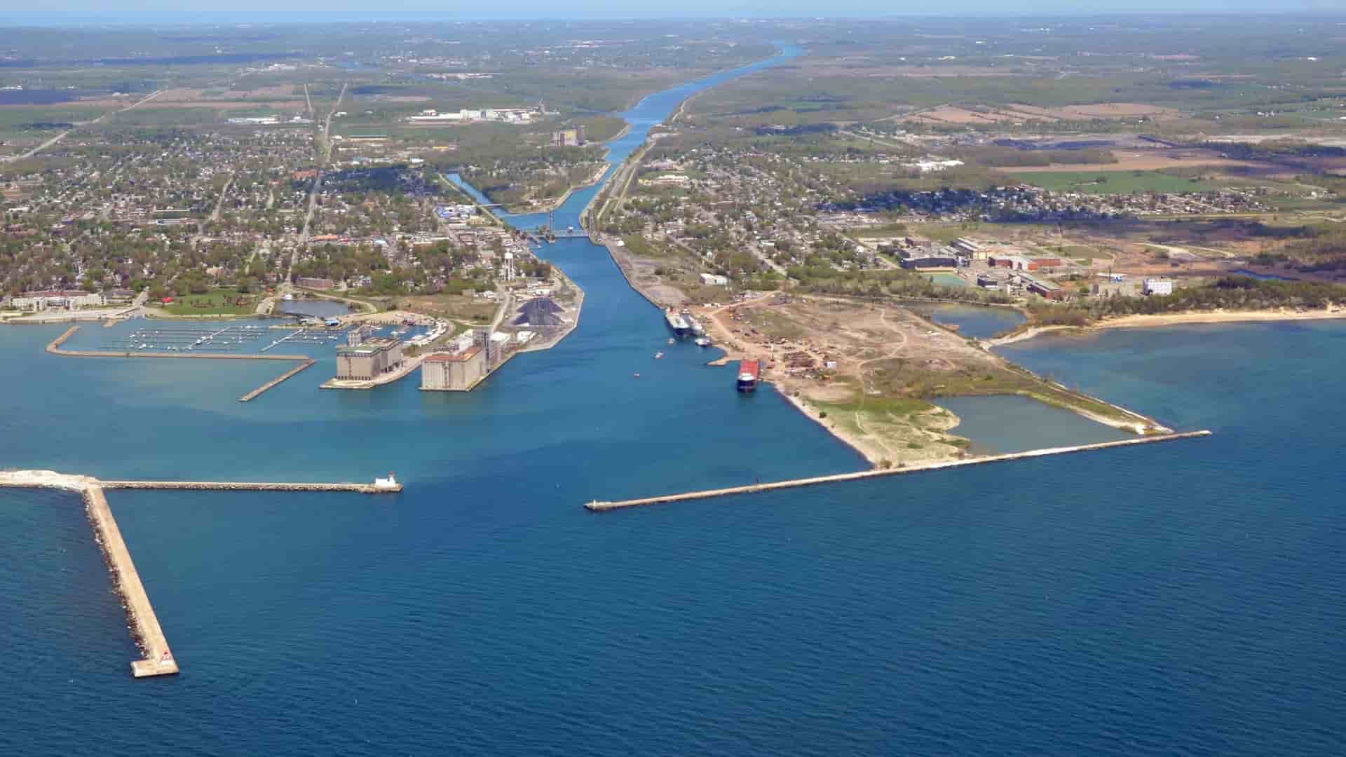 An aerial view of Port Colborne in Ontario, Canada, showing the entrance to the Welland Canal from Lake Erie, with breakwaters, a marina, and industrial buildings along the waterfront.